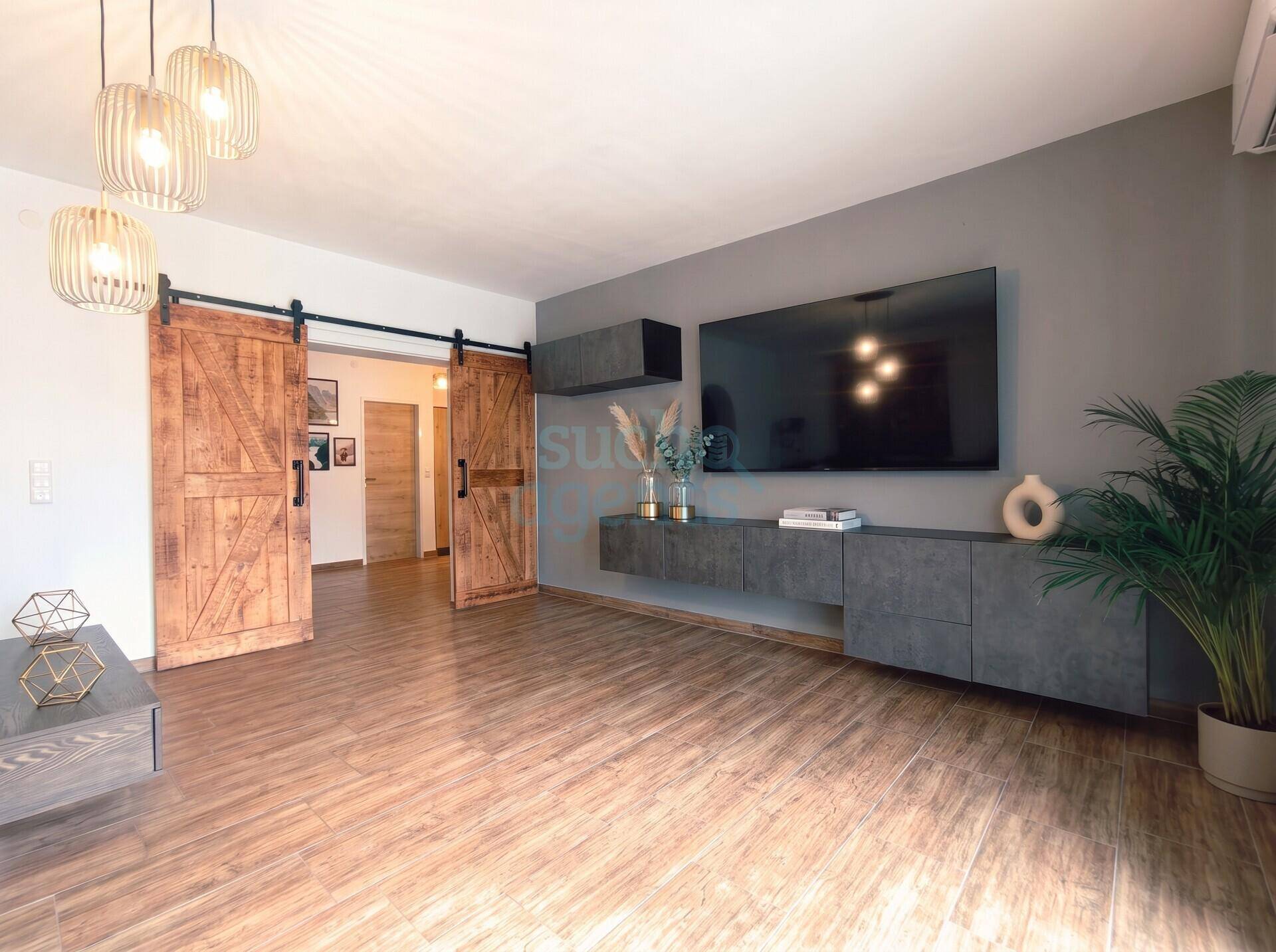 Modernes Wohnzimmer mit Holzboden, großer TV-Wand und rustikalen Schiebetüren aus Holz.