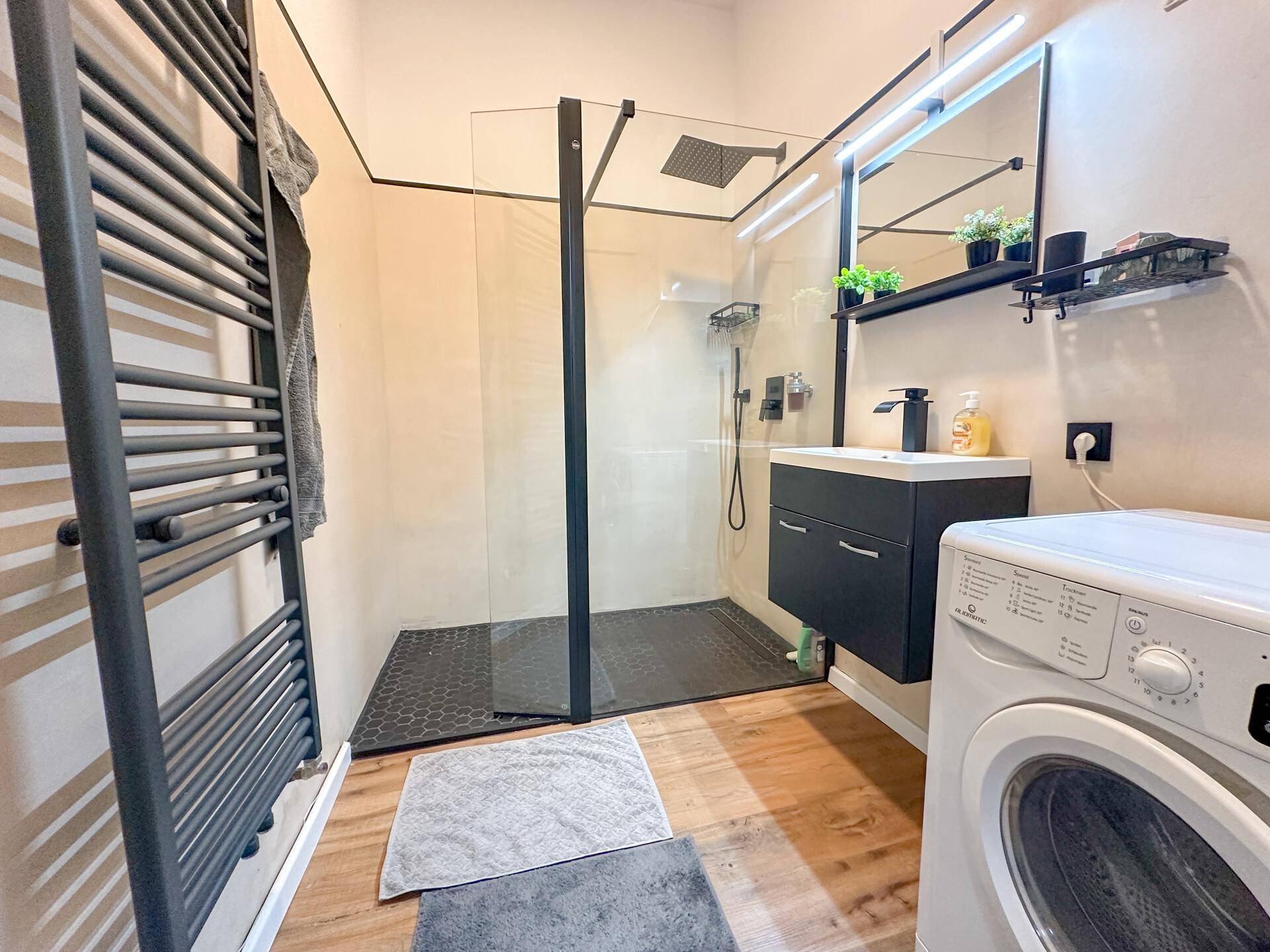 Modernes Badezimmer mit ebenerdiger Dusche, Waschbecken, beheiztem Handtuchhalter und Waschmaschine.