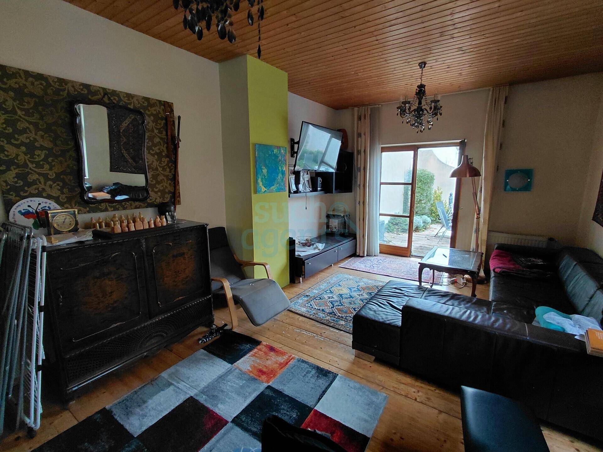 Wohnzimmer mit Holzdecke, Holzboden, bequemer Couch und Zugang zum Garten.