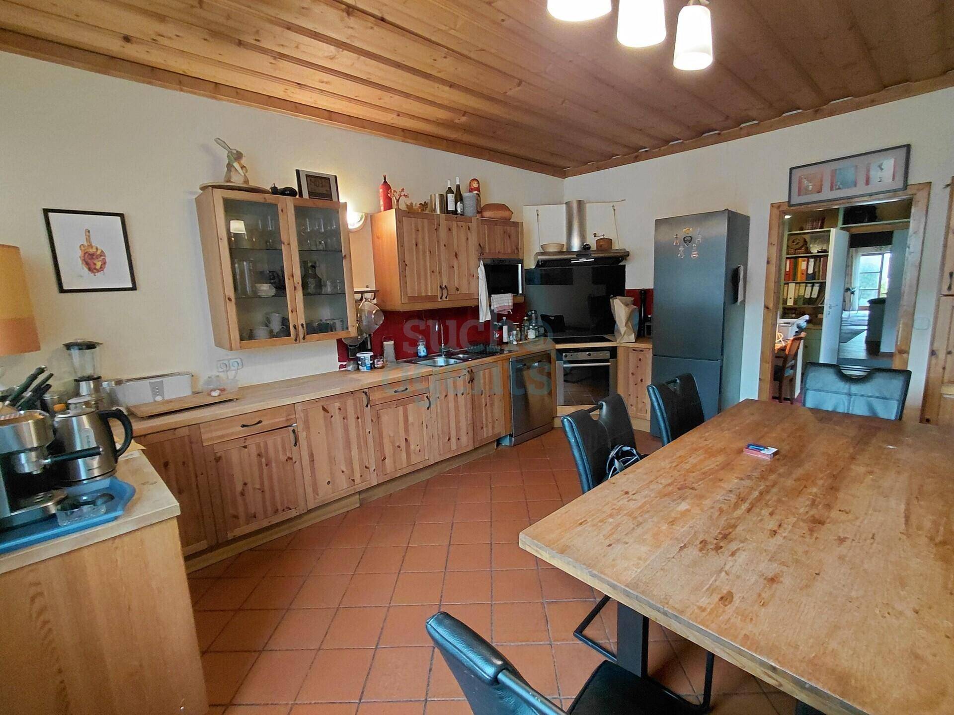 Rustikale Küche mit Holzschränken, Terrakottaboden und einem großen Esstisch.