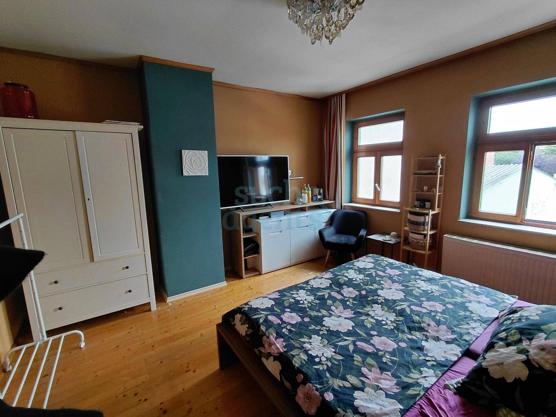 Schlafzimmer mit Holzboden, einem großen Bett und einem weißen Kleiderschrank.
