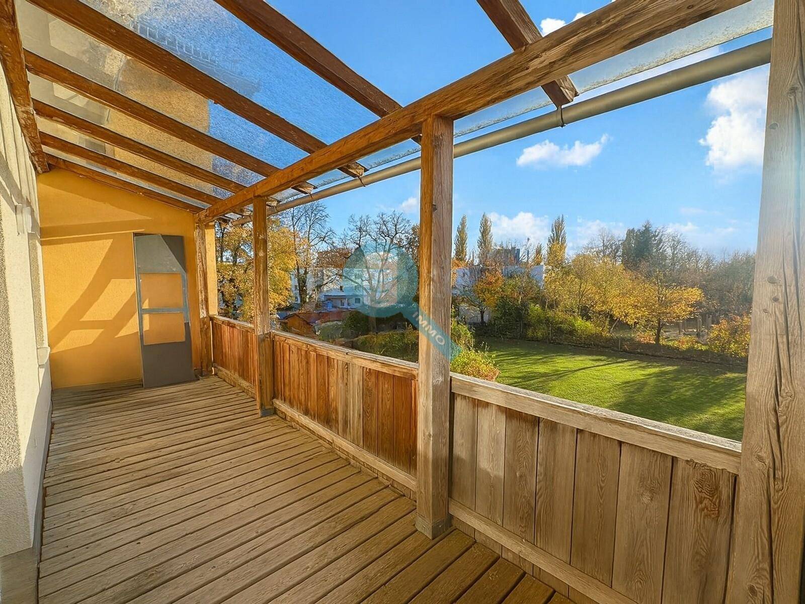Geräumiger überdachter Holzbalkon mit Blick ins Grüne und auf umliegende Häuser.