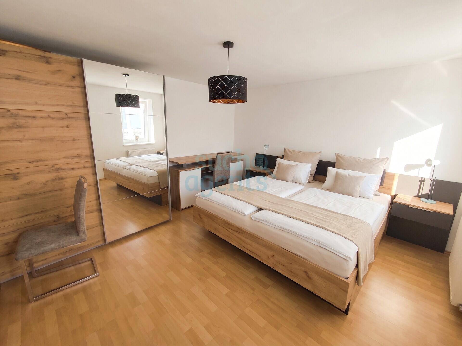 Gemütliches Schlafzimmer mit Doppelbett, Holzboden, großem Spiegelschrank und Schreibtischbereich.