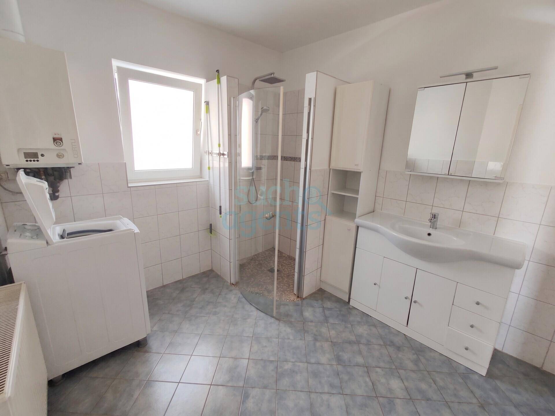 Funktionales Badezimmer mit Dusche, Waschbecken, Waschmaschine und Fenster.