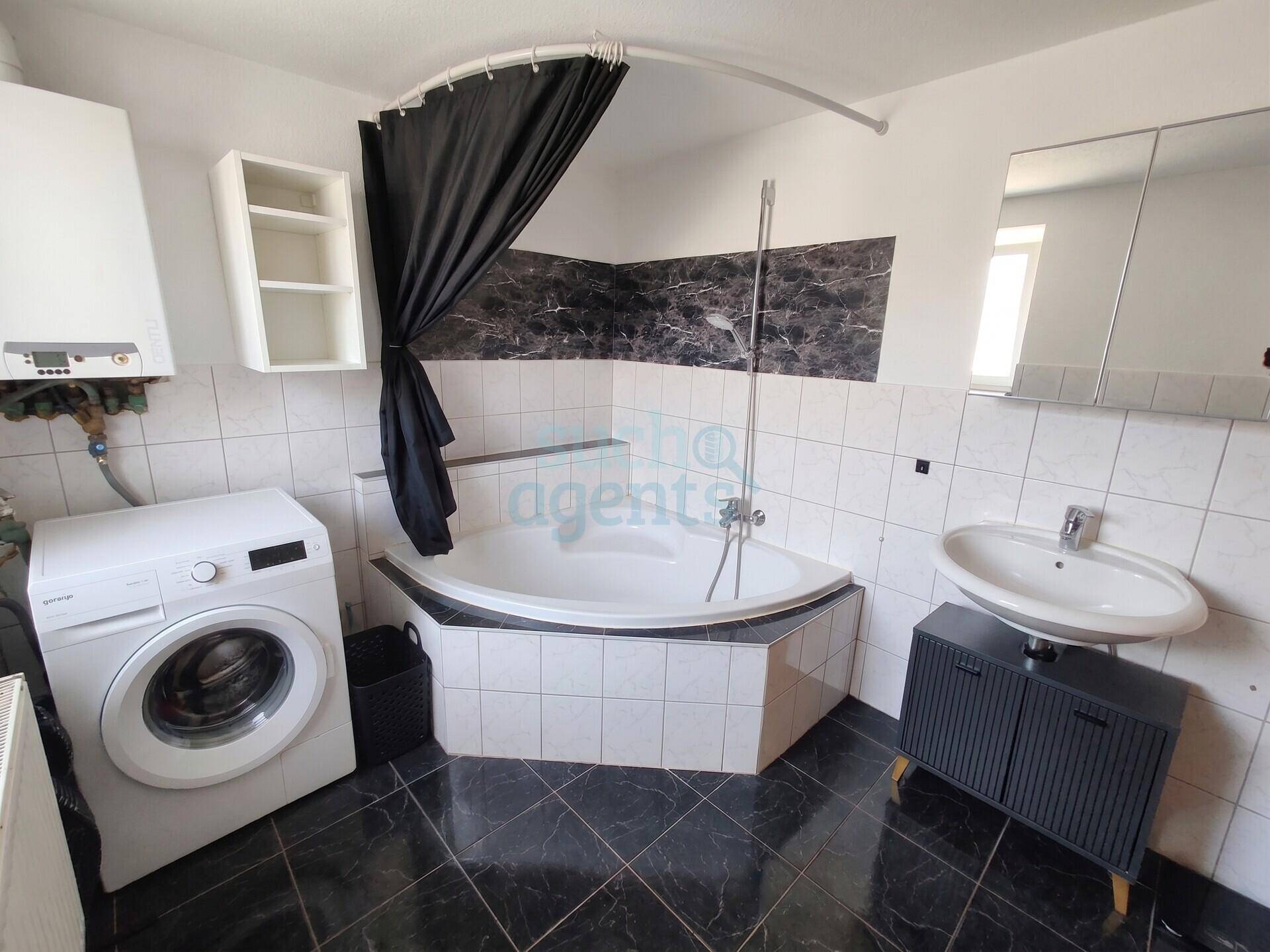 Badezimmer mit Eckbadewanne, Waschmaschine und Waschbecken.