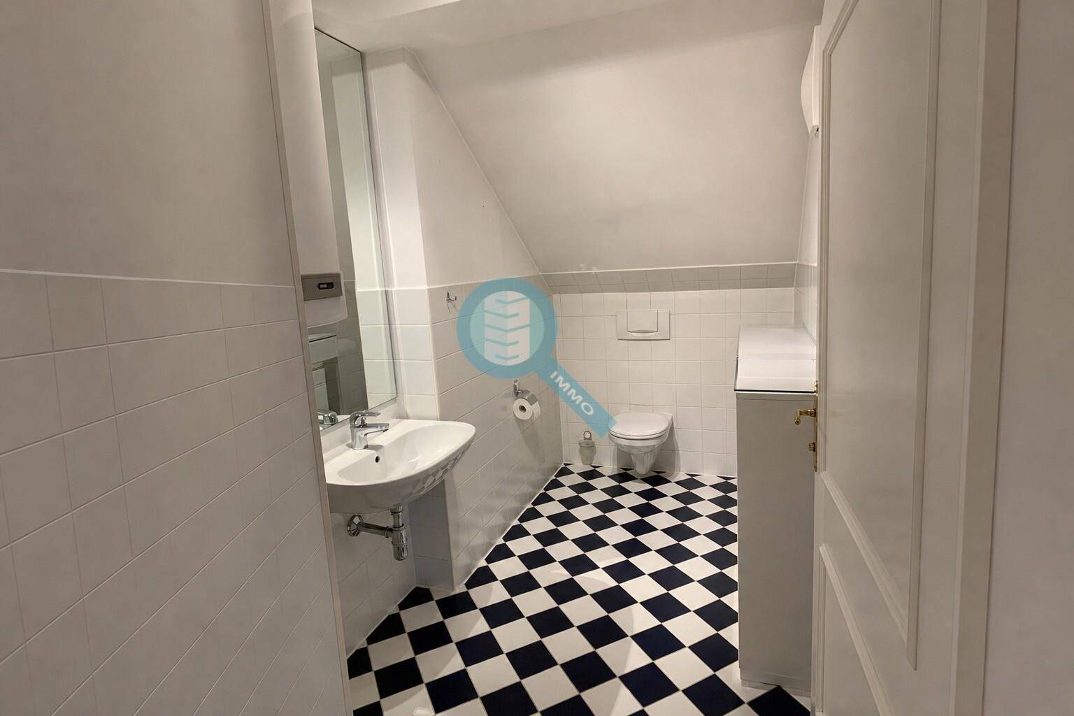 Badezimmer mit WC, Waschbecken, Spiegel und charakteristischen schwarz-weißen Fliesen.