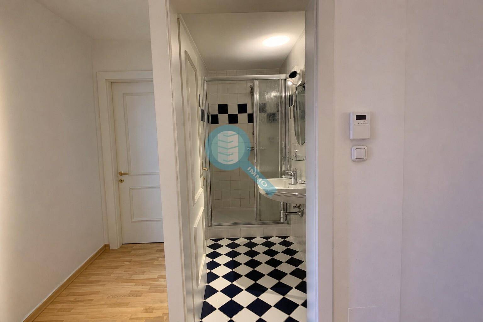 Badezimmer mit schwarz-weiß karierten Fliesen, Duschkabine und Waschbecken.