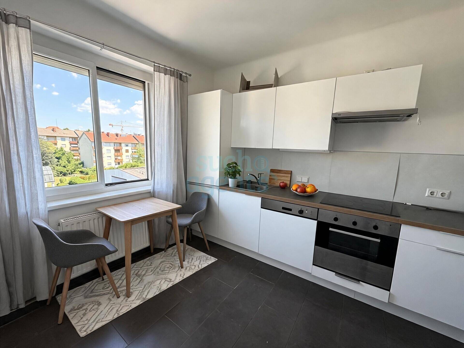 Moderne Einbauküche mit weißen Schränken, dunklem Fliesenboden und einem kleinen Essbereich am Fenster.