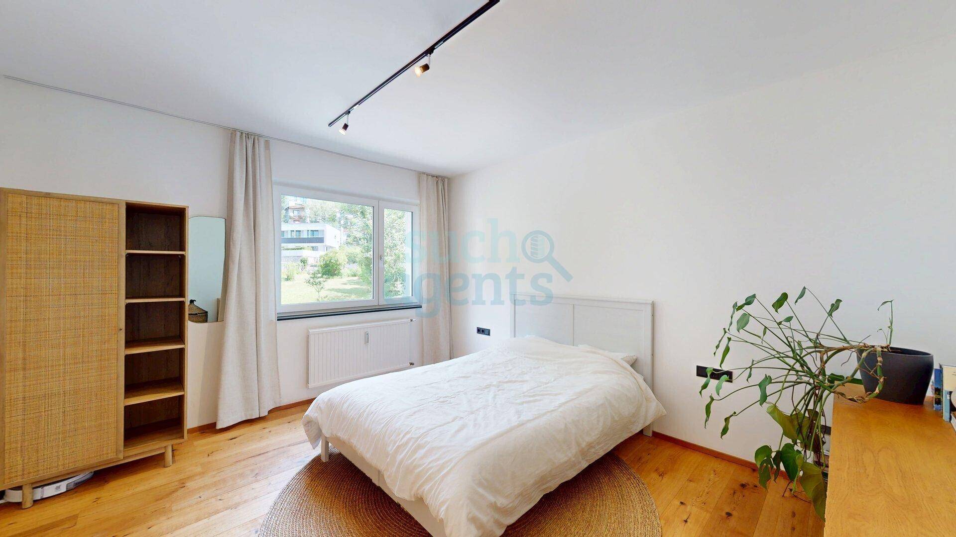 Helles Schlafzimmer mit Holzboden, großem Fenster und schlichtem, modernem Design.