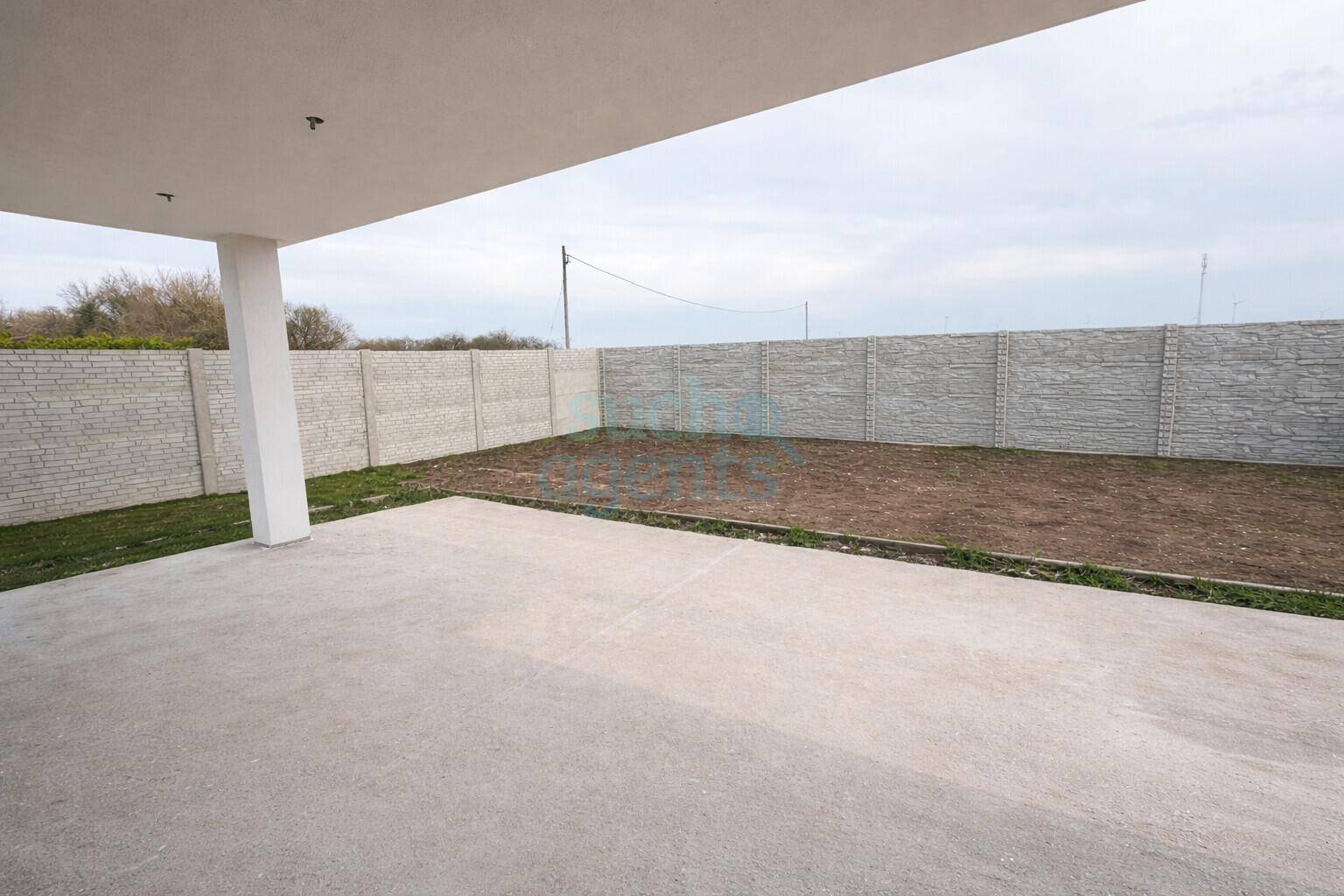 Großzügige Beton-Terrasse mit Blick auf den umzäunten Gartenbereich und Betonmauer.