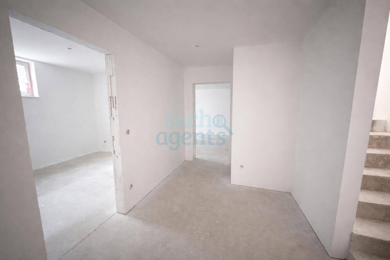Unmöblierter Flur mit Rohbauwänden und Betontreppe, die zu weiteren Etagen führt.