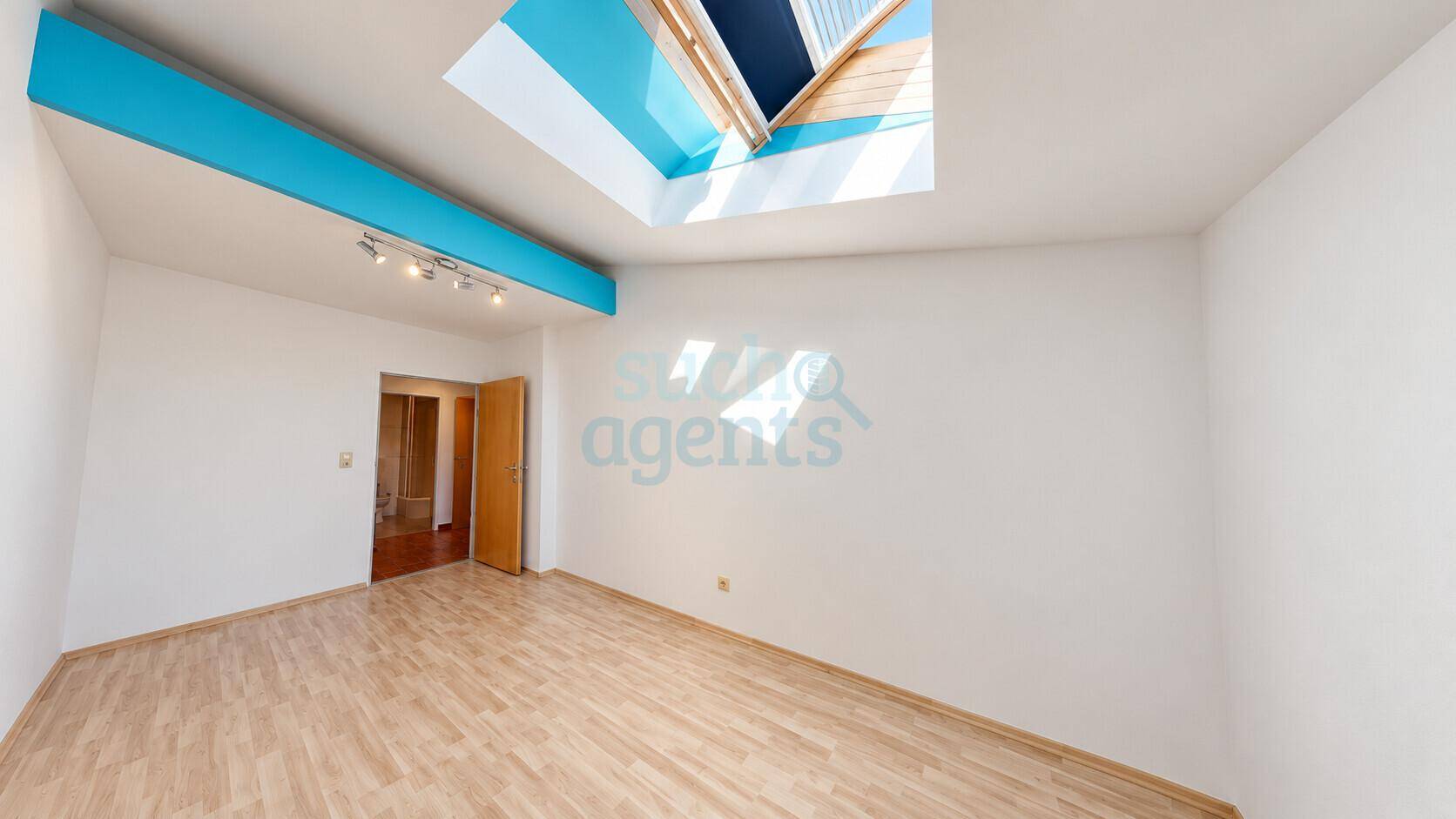 Heller, leerer Raum mit großem Dachfenster und blauer Deckenleiste, ideal für verschiedene Nutzungen.