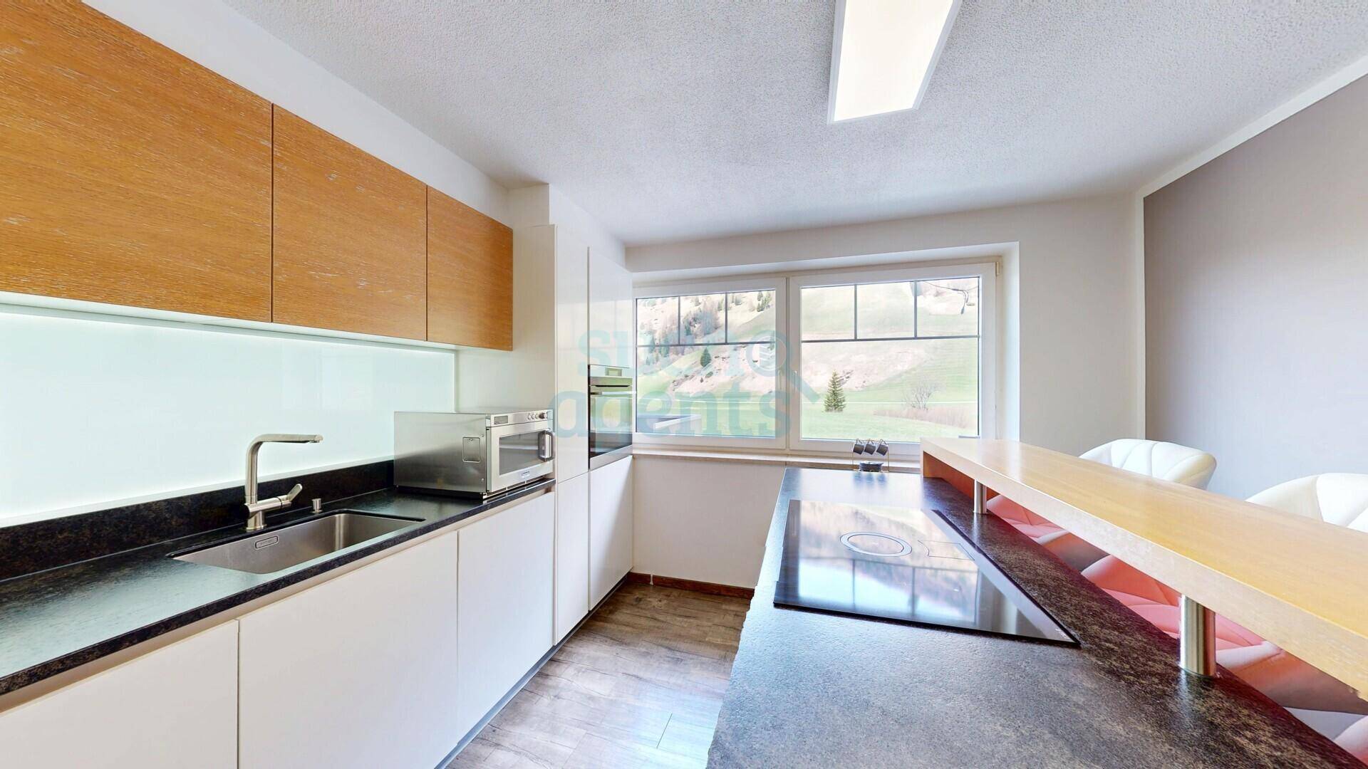 Moderne Küche mit weißen Unterschränken, Holzakzenten, Kochinsel und Fenster mit Bergblick.
