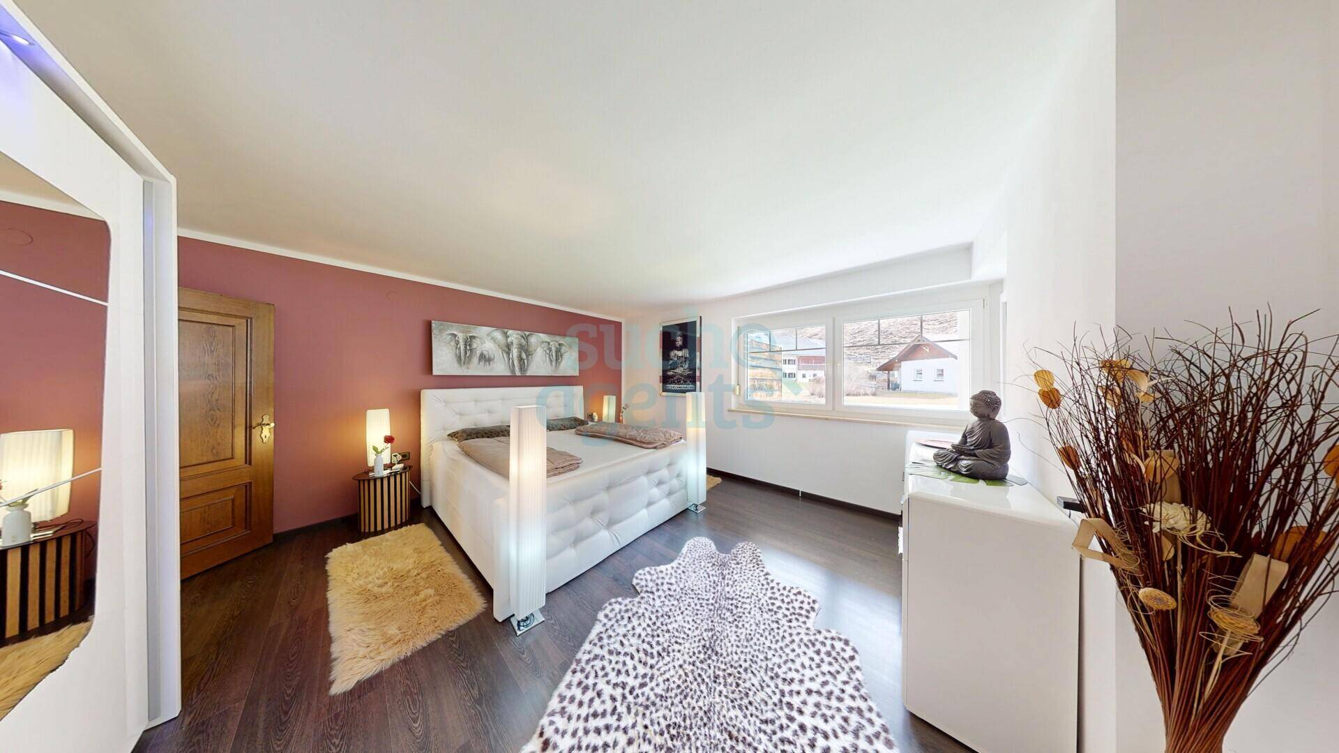 Gemütliches Schlafzimmer mit Holzboden, großem Bett und Blick ins Grüne.