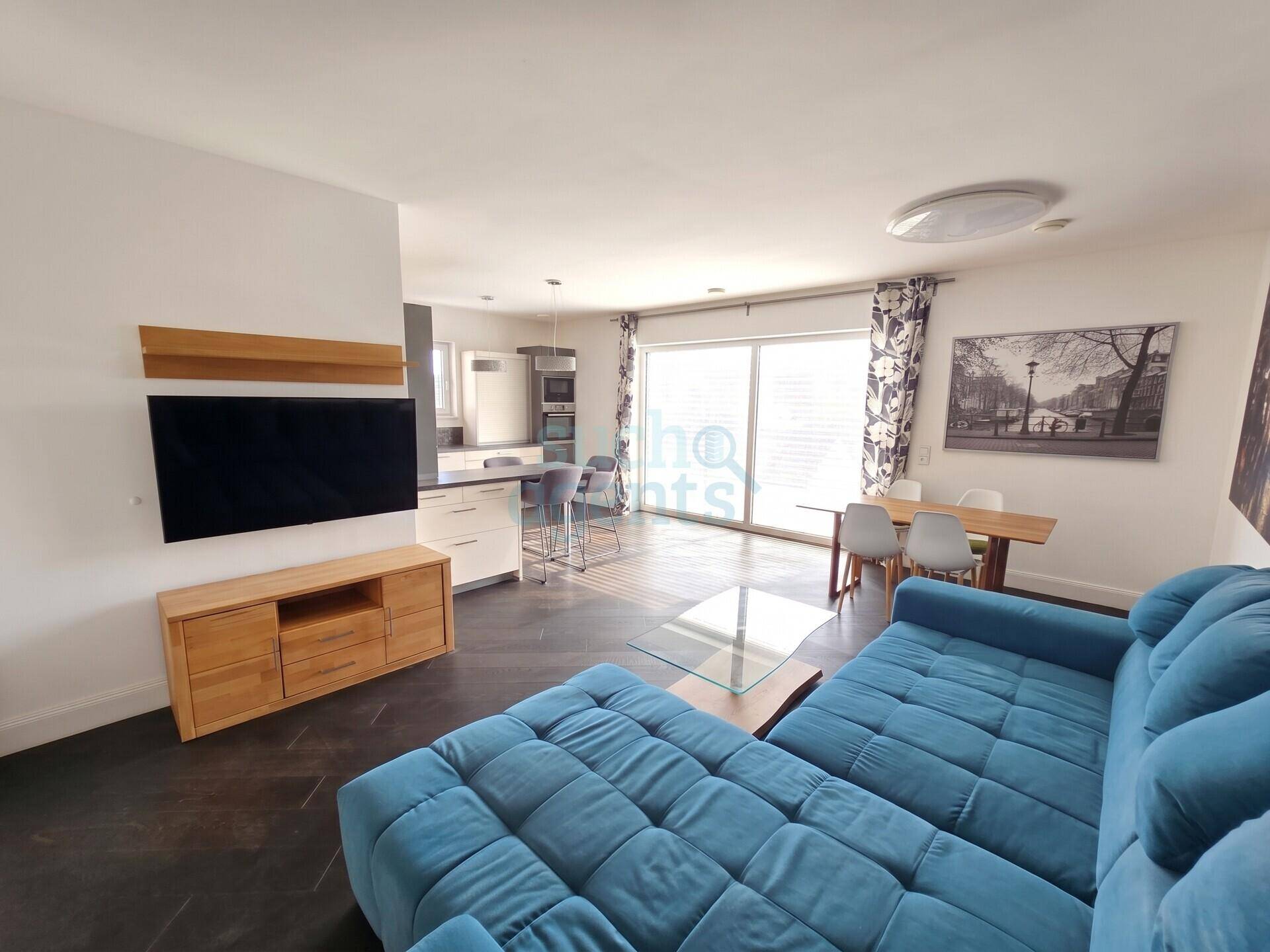 Offener Wohn-Essbereich mit moderner Küche, großem Sofa und Zugang zu einem Balkon oder einer Terrasse.