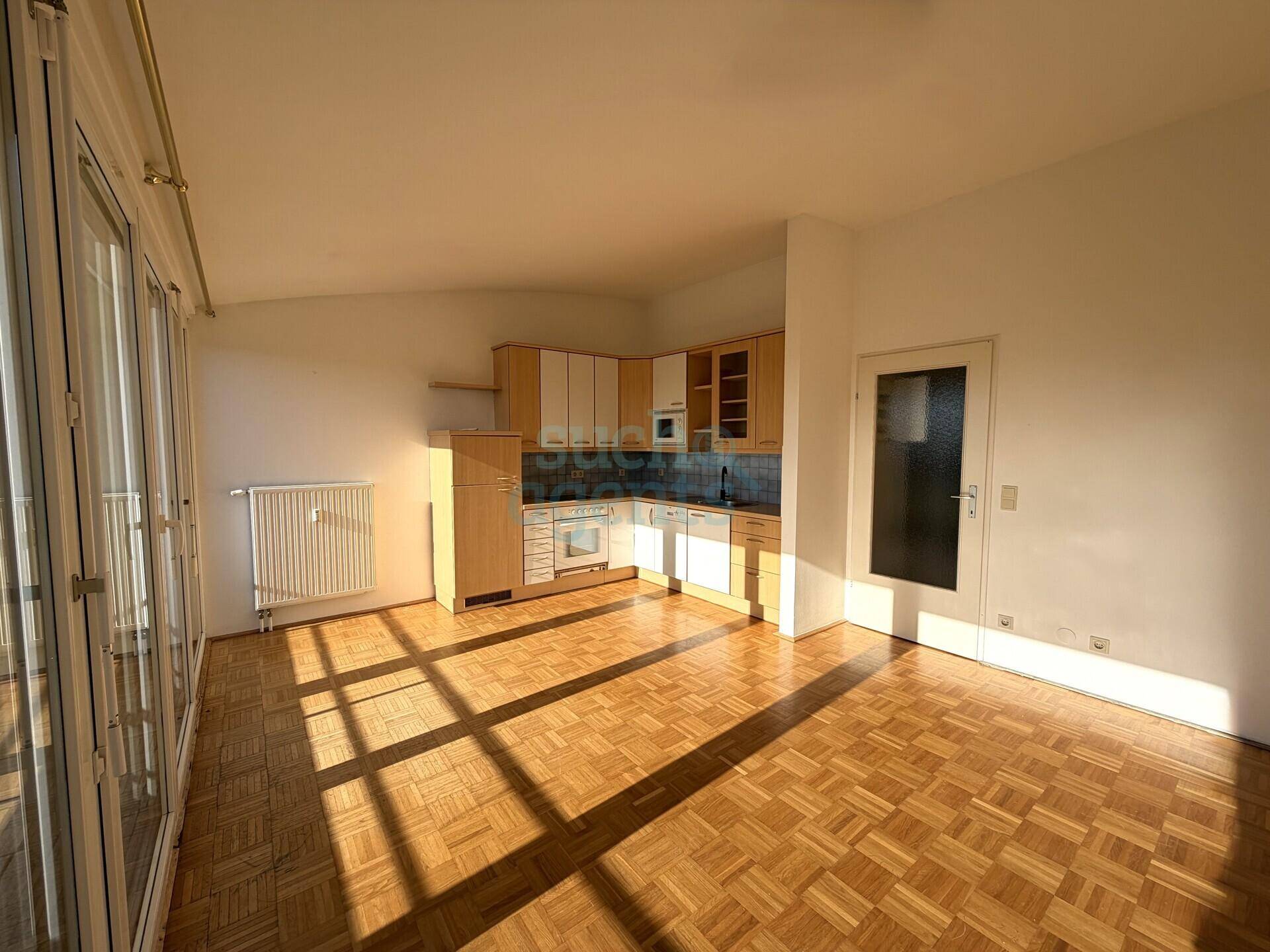 Heller Wohnbereich mit integrierter Küchenzeile, Parkettboden und Zugang zum Balkon.