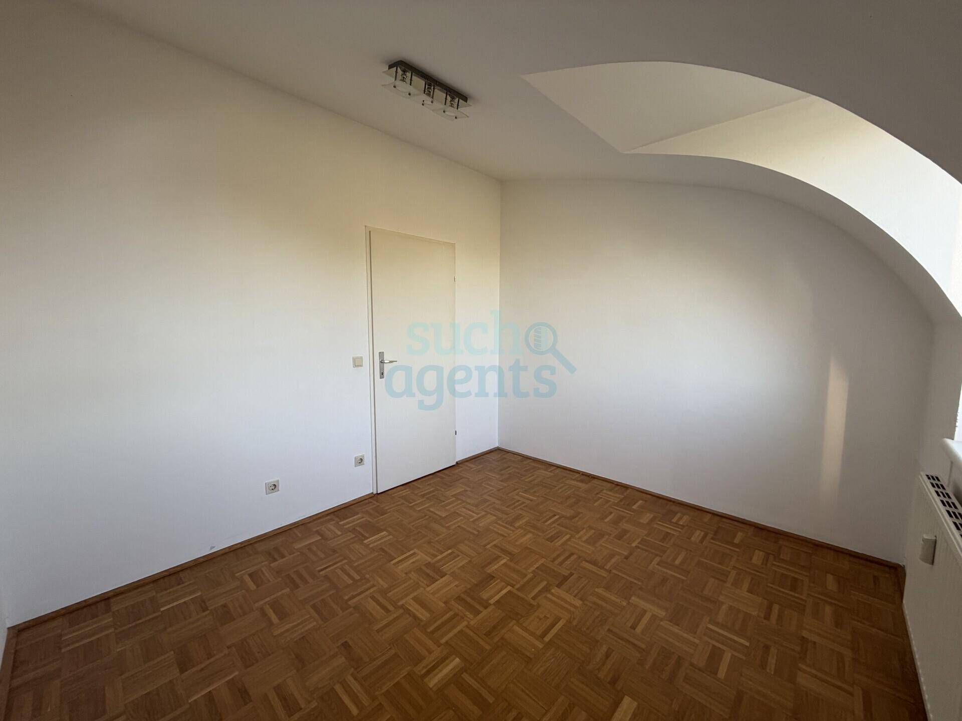 Leeres Zimmer im Dachgeschoss mit Parkettboden, weiß gestrichenen Wänden und Dachschräge.