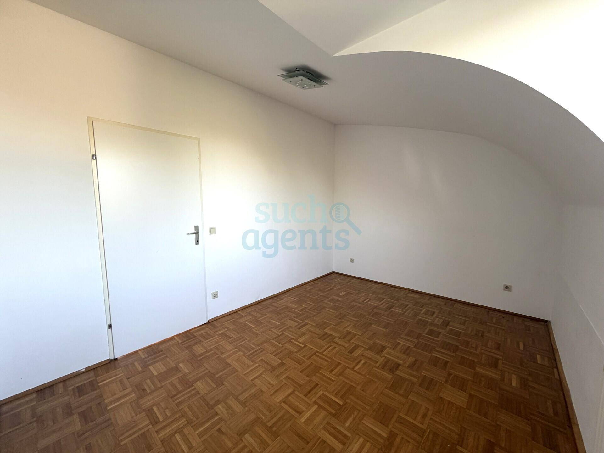 Helles Zimmer mit Parkettboden, Dachschräge und weißer Tür, ideal als Schlaf- oder Arbeitszimmer.