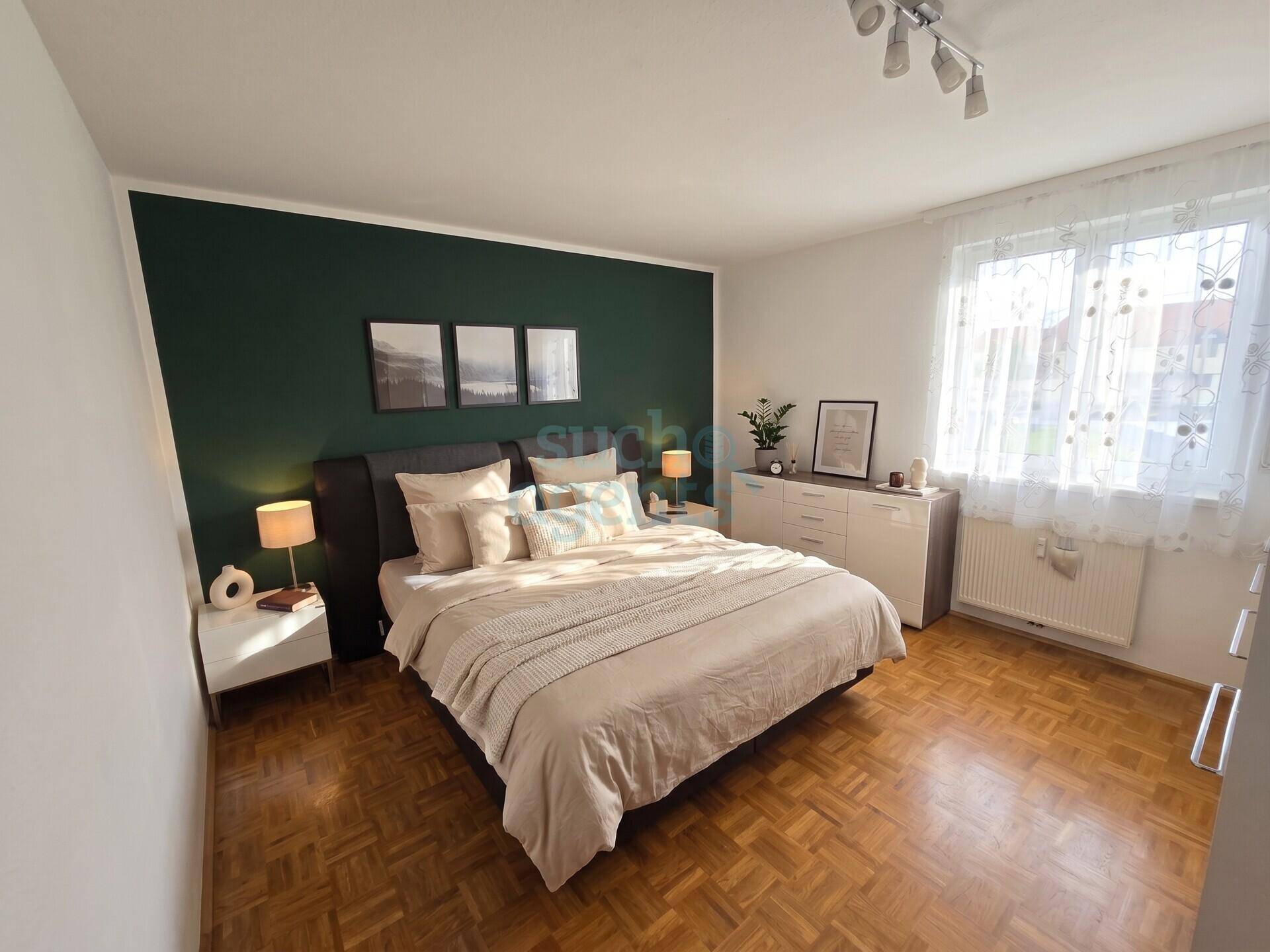 Gemütliches Schlafzimmer mit Parkettboden, grüner Akzentwand und großem Fenster.