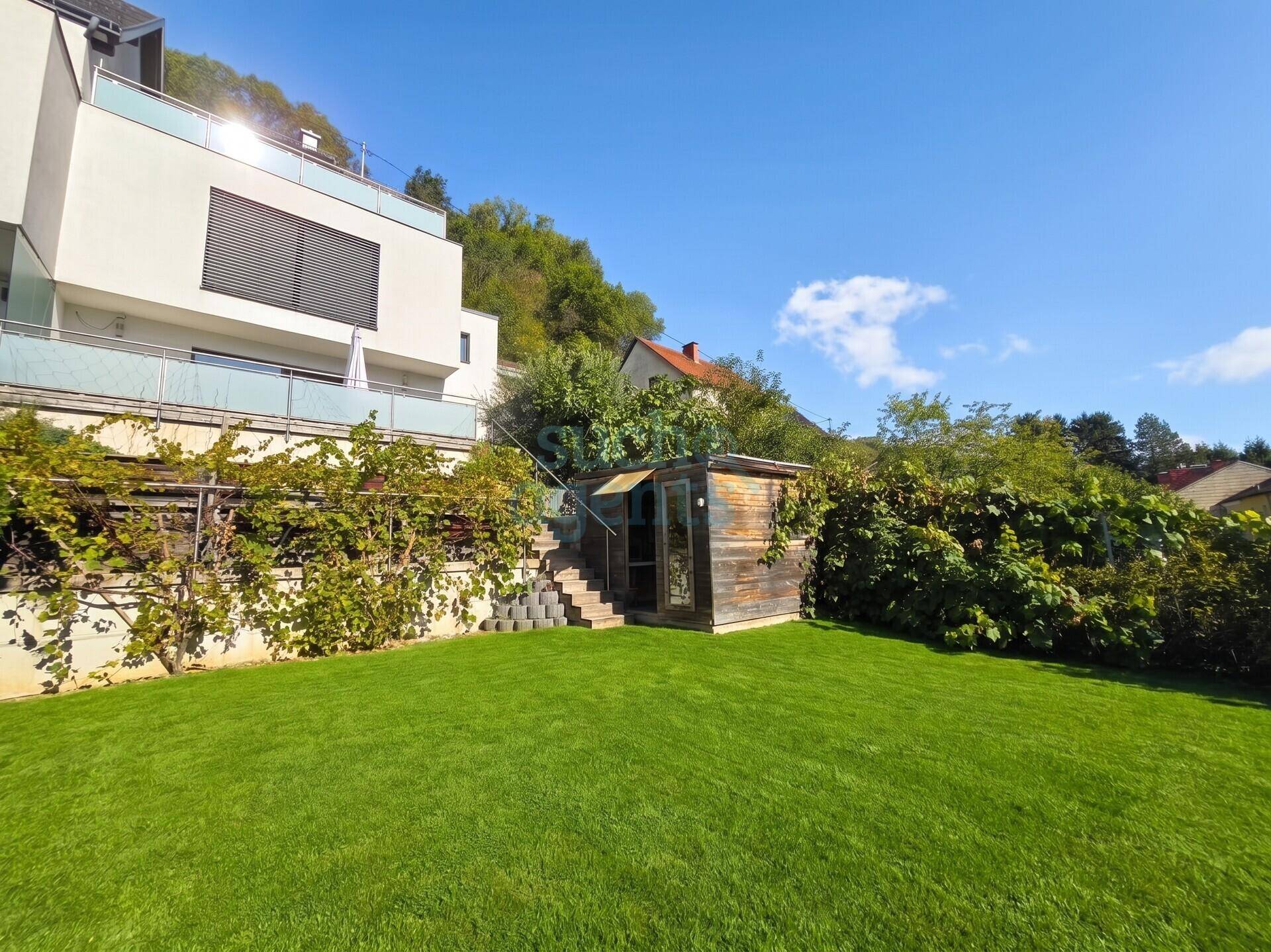 Gepflegter Rasenbereich mit Gartenhaus und Blick auf die moderne Architektur des Gebäudes.