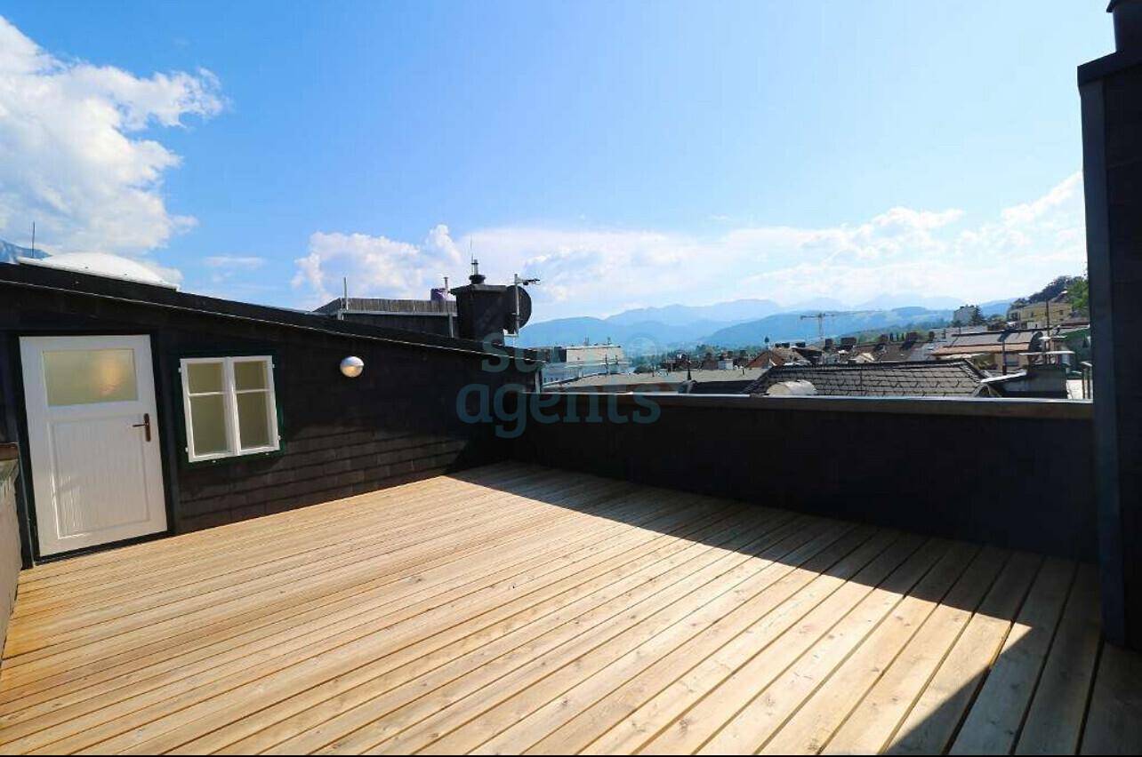 Große, unmöblierte Dachterrasse mit Holzboden und Panoramablick über die Stadt und Berge.