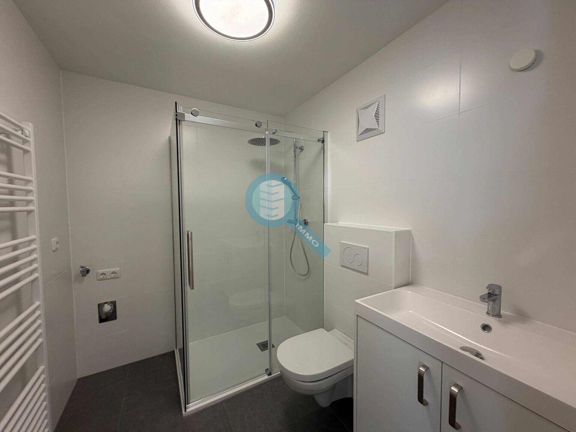 Modernes Badezimmer mit ebenerdiger Dusche, WC, Waschbecken und einem beheizten Handtuchhalter.