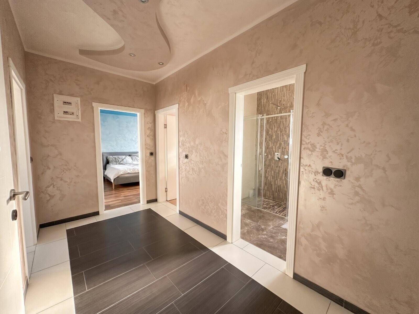 Heller Flur mit dunklen Fliesen, der zu Schlafzimmer und Badezimmer führt.