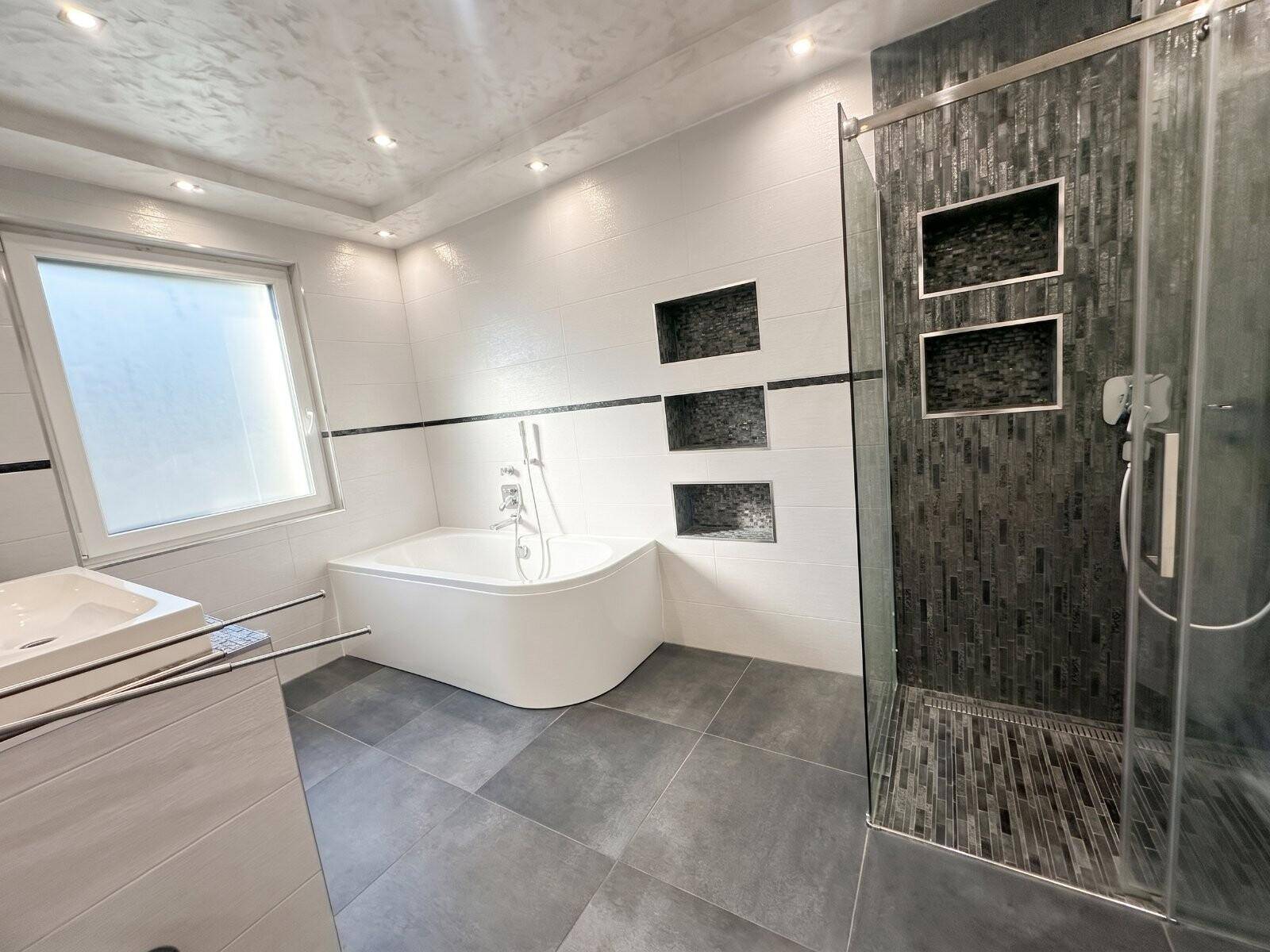 Modernes Badezimmer mit Eckbadewanne, Duschkabine und großformatigen Fliesen.