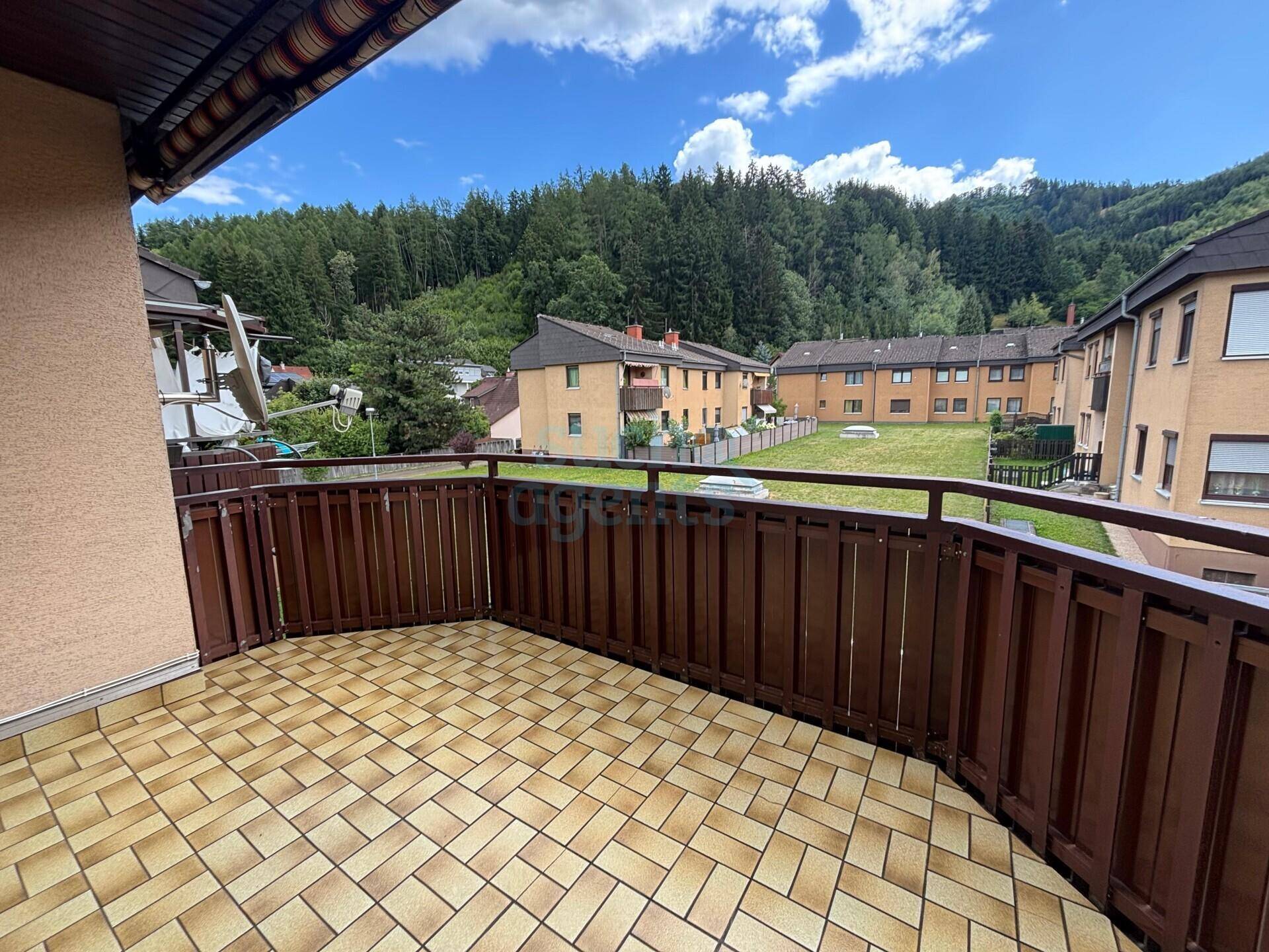 Geräumiger Balkon mit Fliesenboden, Holzgeländer und weitem Blick auf bewaldete Hügel.