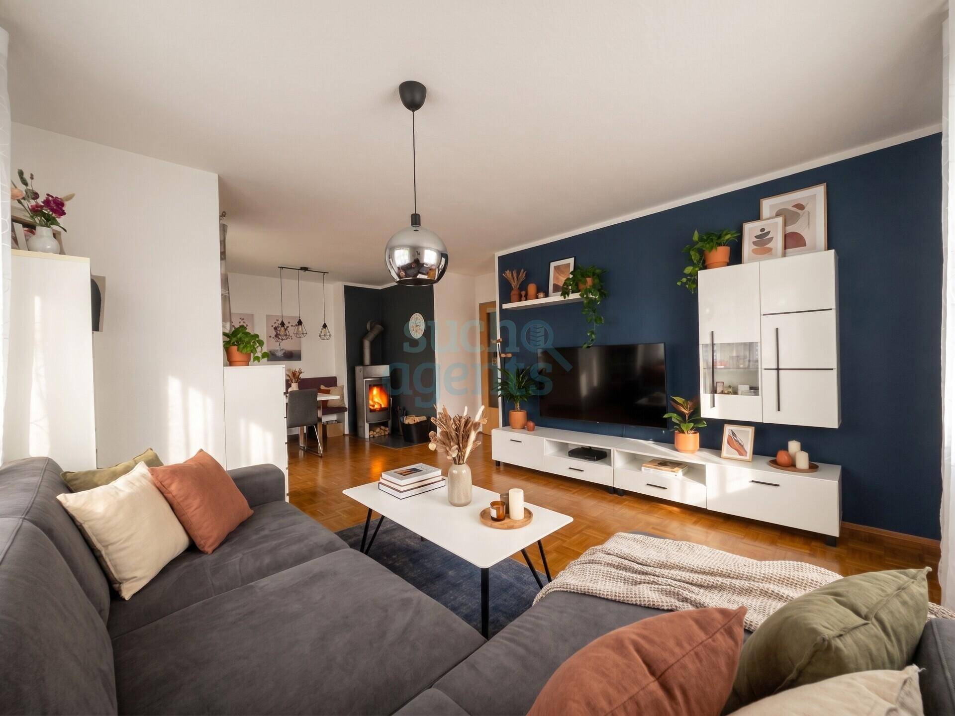 Geräumiger Wohnbereich mit Sofa, Fernseher und Essbereich im Hintergrund, inklusive Kaminofen.