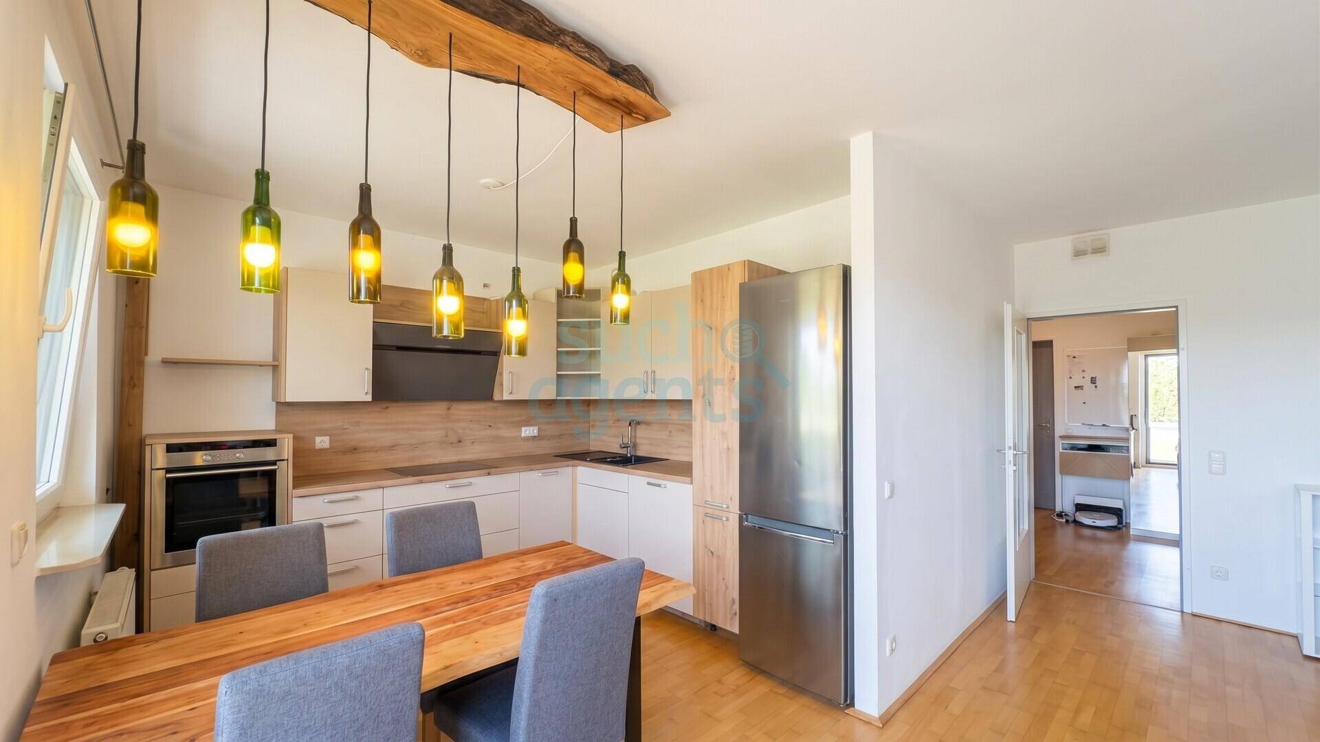 Moderne Küche mit Holzakzenten, Essbereich und Edelstahlgeräten, offen zum Wohnbereich.