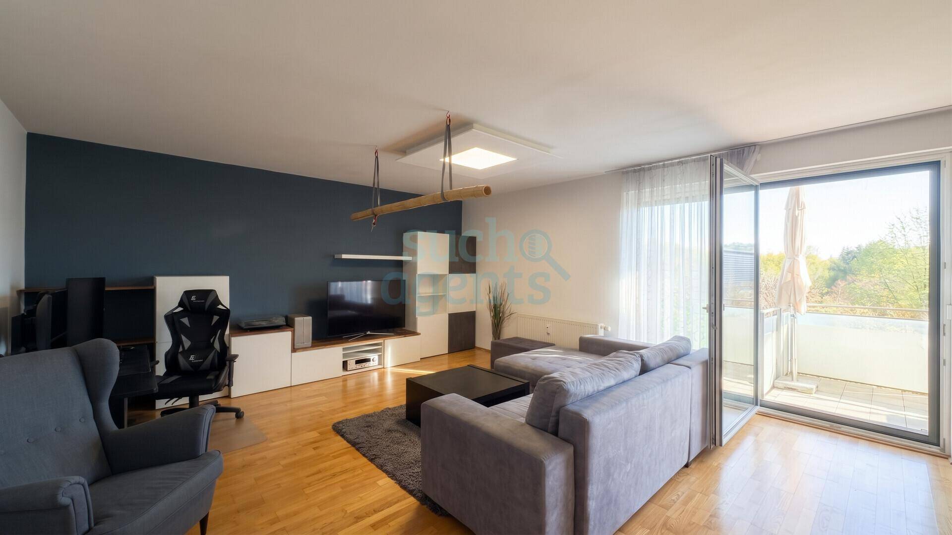 Helles Wohnzimmer mit Holzboden, Zugang zum Balkon und moderner Unterhaltungselektronik.