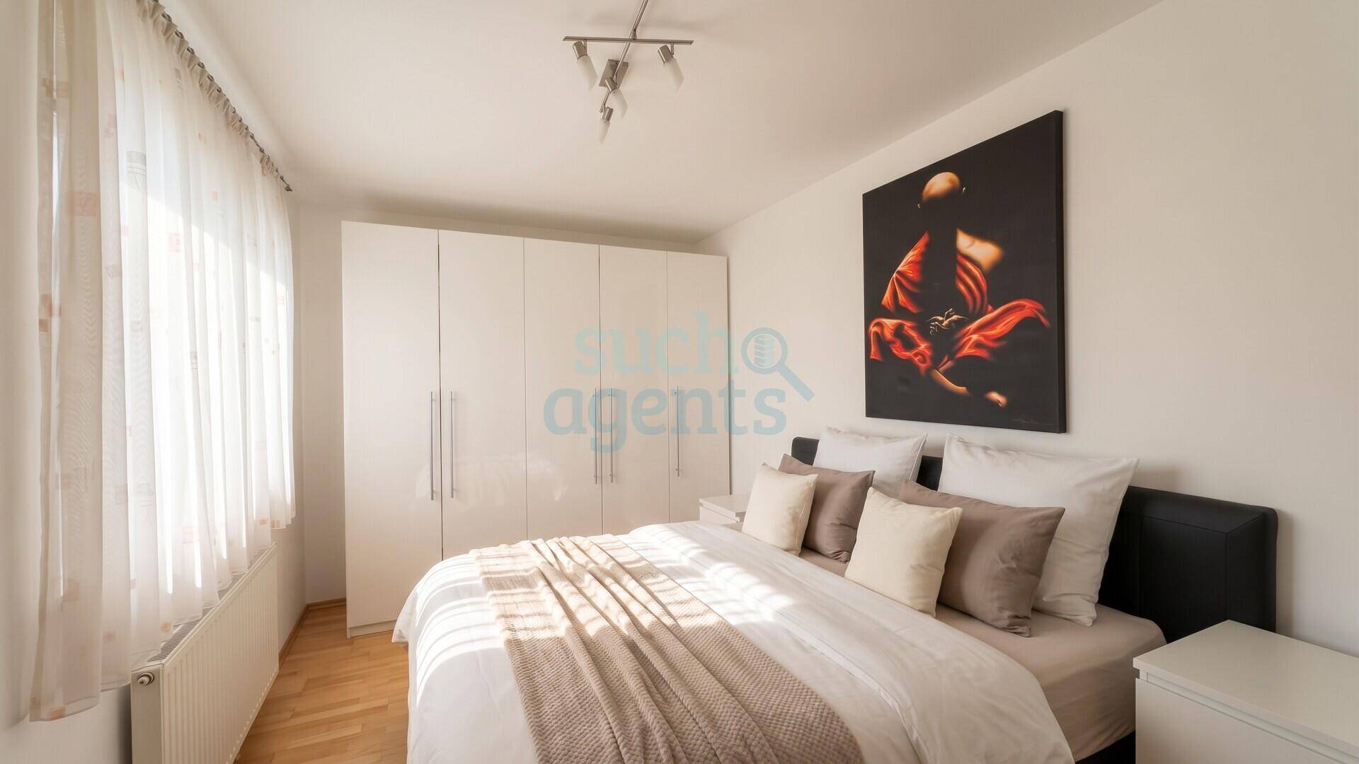 Gemütliches Schlafzimmer mit Doppelbett, weißen Einbauschränken und großem Fenster für viel Licht.