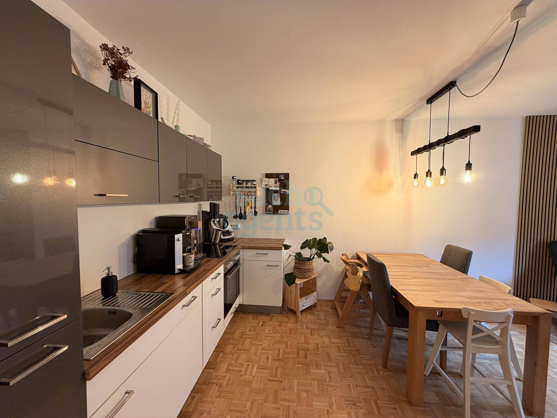 Moderne Küche mit grauen Oberschränken, Holzarbeitsplatte und Essbereich.
