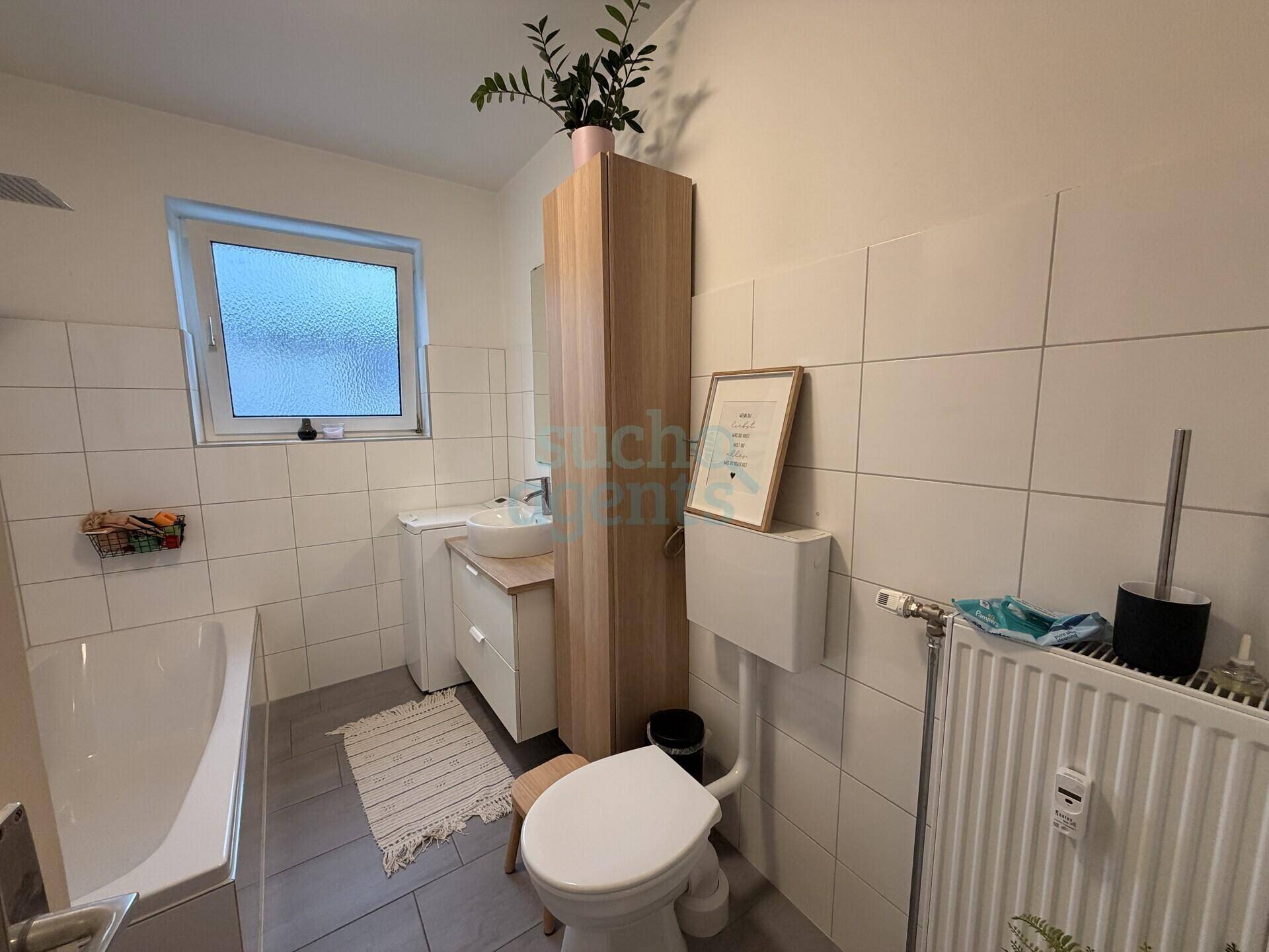 Helles Badezimmer mit Badewanne, WC, Waschbecken und Fenster.