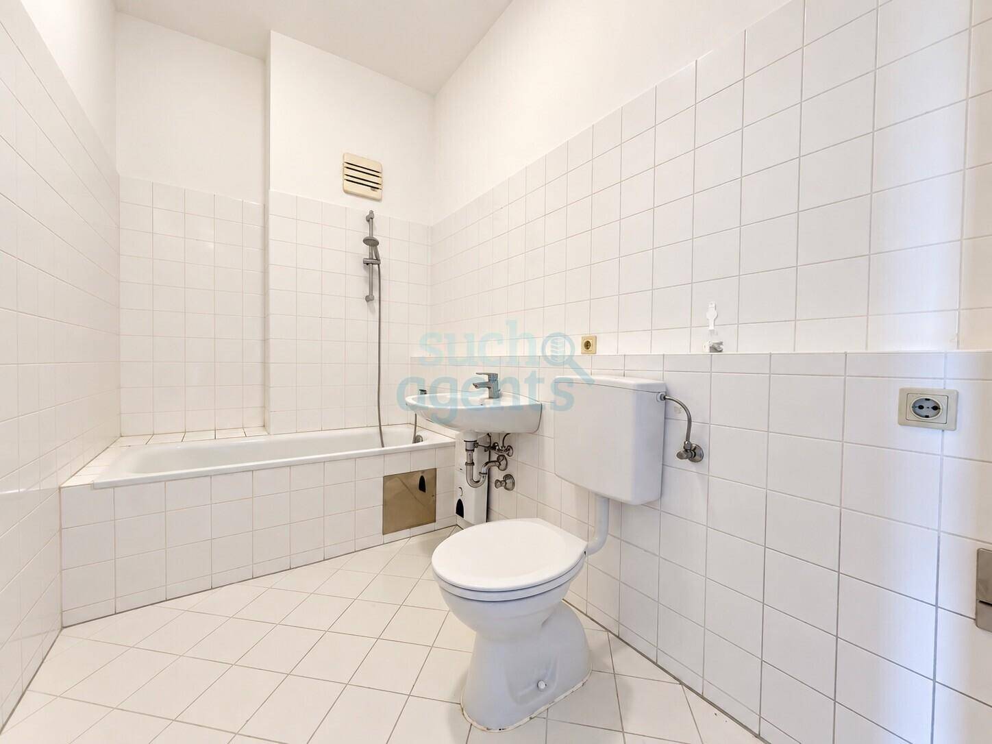 Funktionales Badezimmer mit weißen Fliesen, Badewanne, Toilette und kleinem Waschbecken.