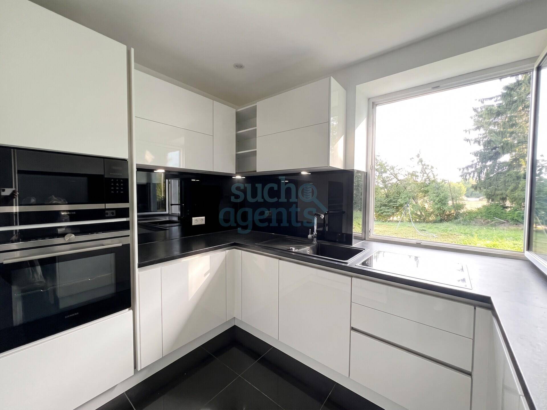 Moderne weiße Küche mit Hochglanzfronten, schwarzen Arbeitsplatten und großem Fenster mit Grünblick.