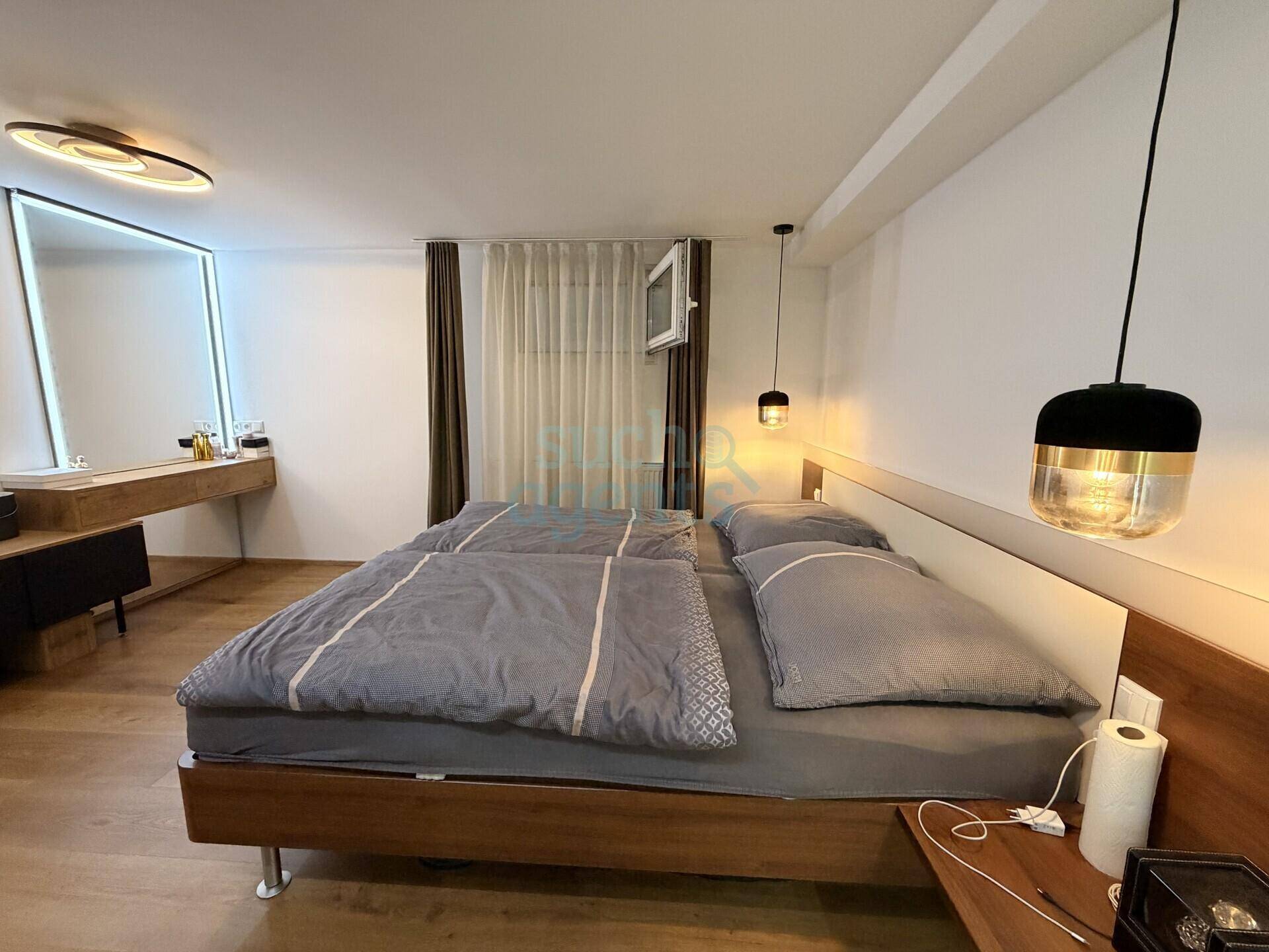 Helles Schlafzimmer mit Doppelbett, modernen Leuchten und einem stilvollen Schminkbereich.