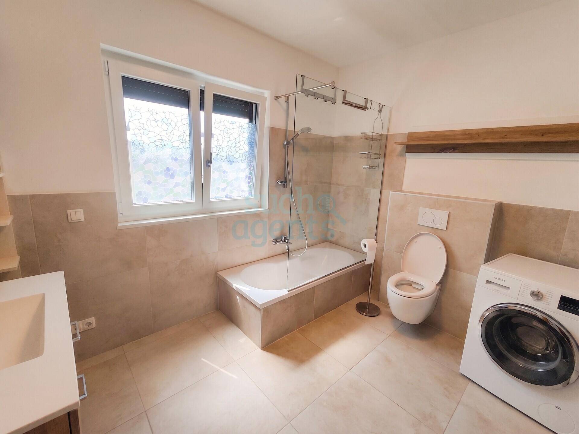 Modernes Badezimmer mit Badewanne, WC, Waschbecken und Waschmaschine, hell gefliest.