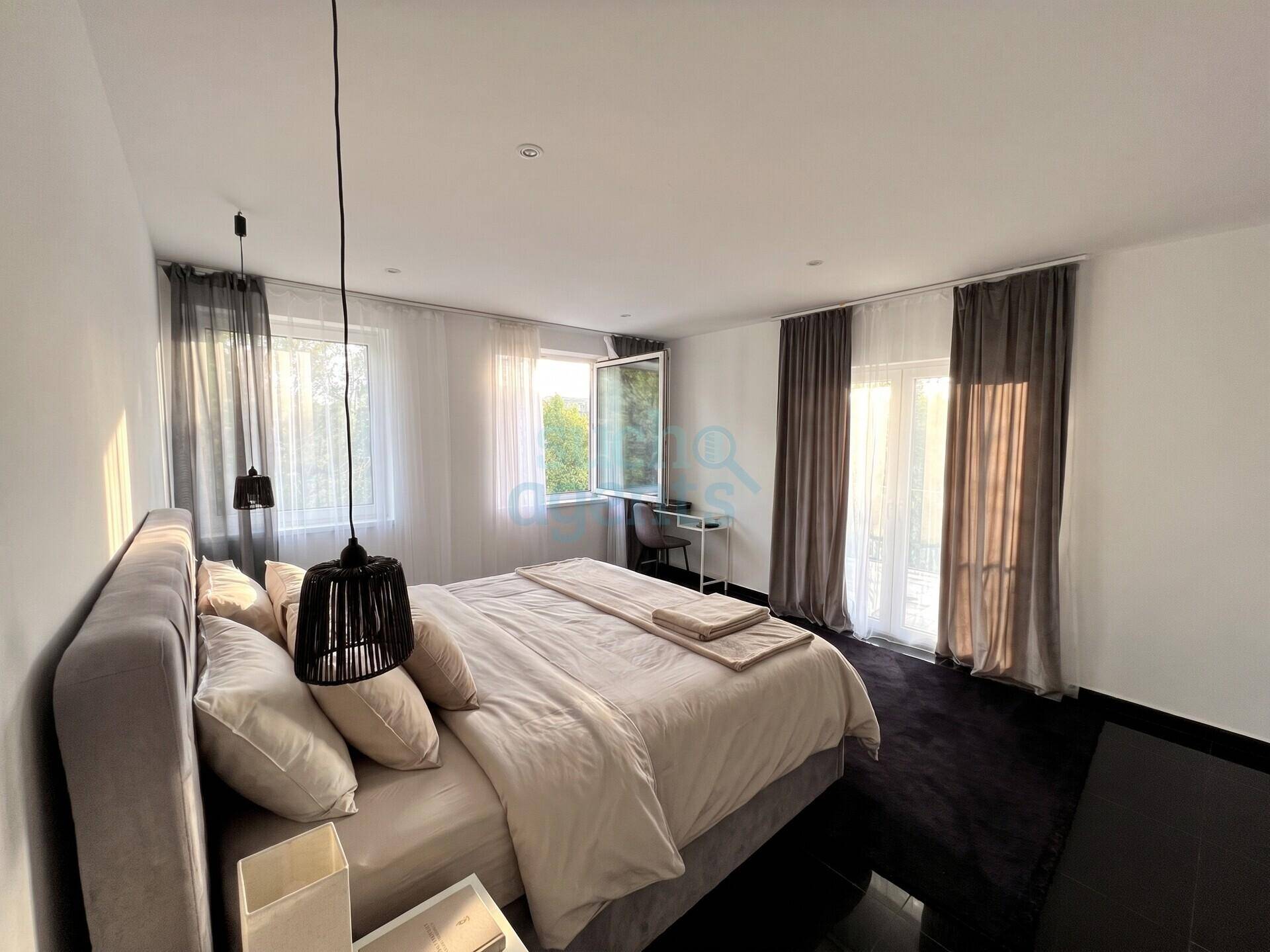 Gemütliches Schlafzimmer mit großem Bett, dunklem Fliesenboden und Zugang zu einem Balkon.