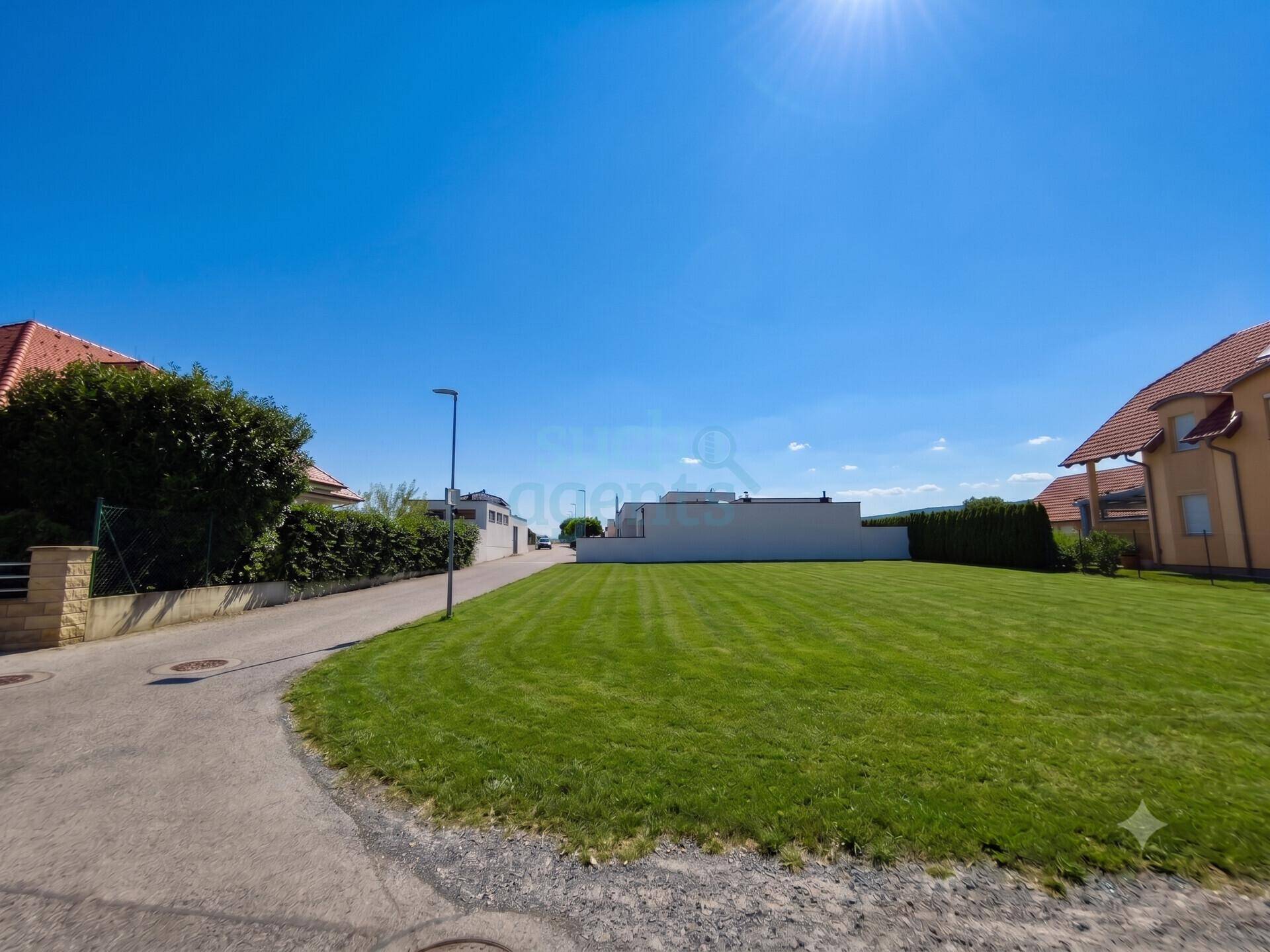 Sonniges Grundstück mit weitläufiger Rasenfläche und Zufahrtsstraße in ruhiger Umgebung.