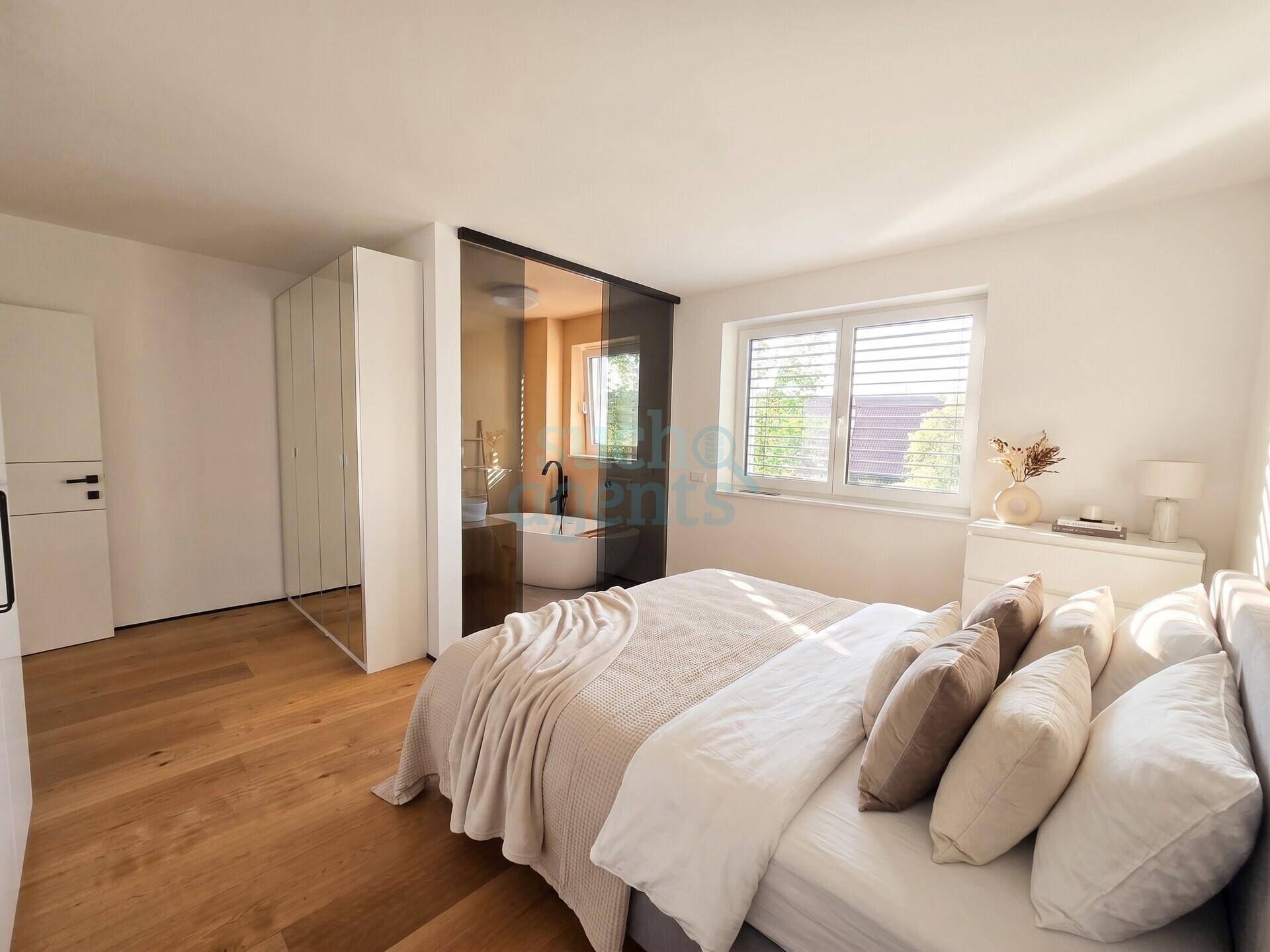 Schlafzimmer mit Eichenparkett und einem elegant integrierten Badezimmerbereich hinter Glaswänden.