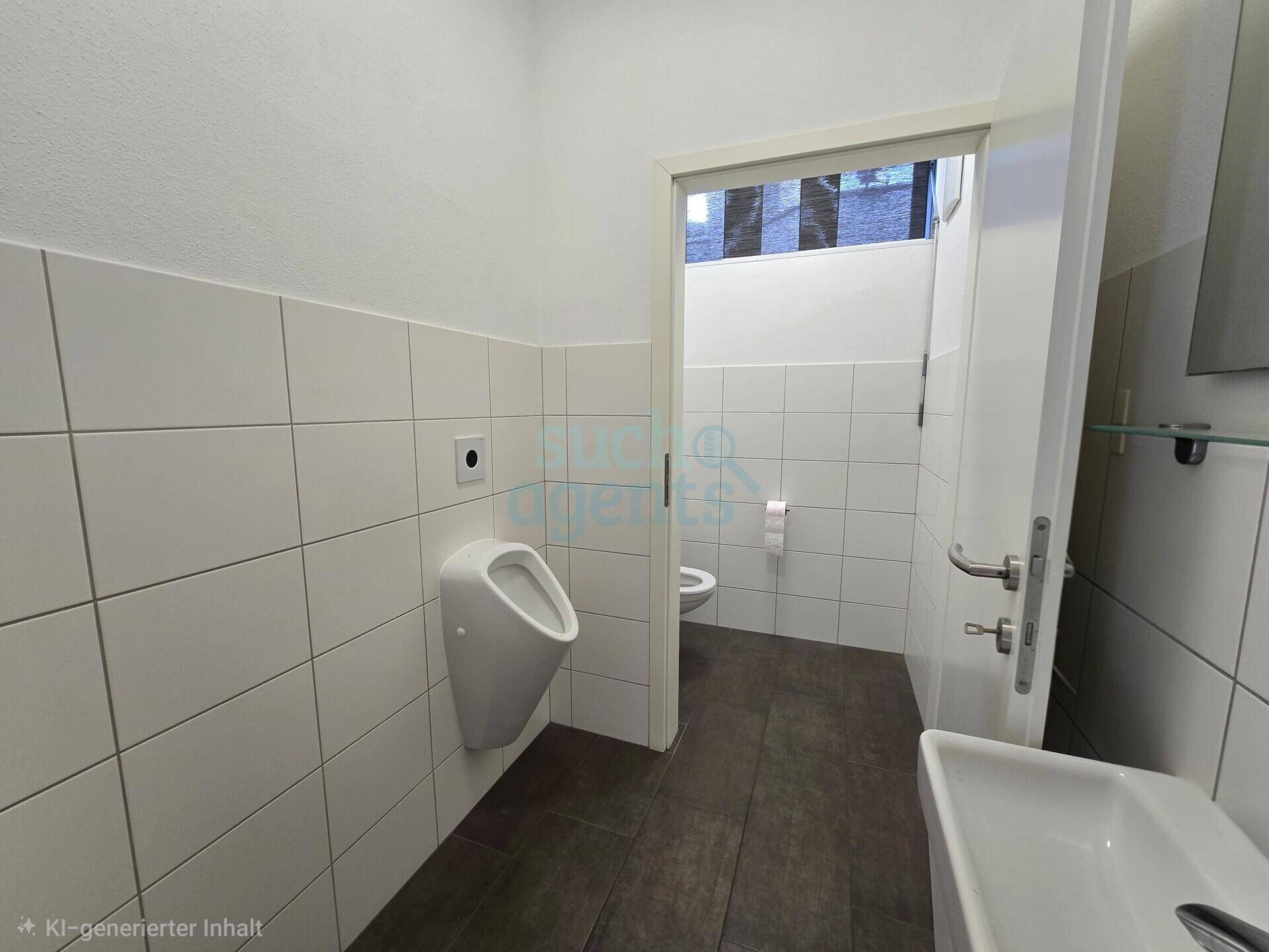 Helle Toilette mit weißen Fliesen, einem Urinal und einem Waschbecken, ausgestattet mit dunklem Fliesenboden.