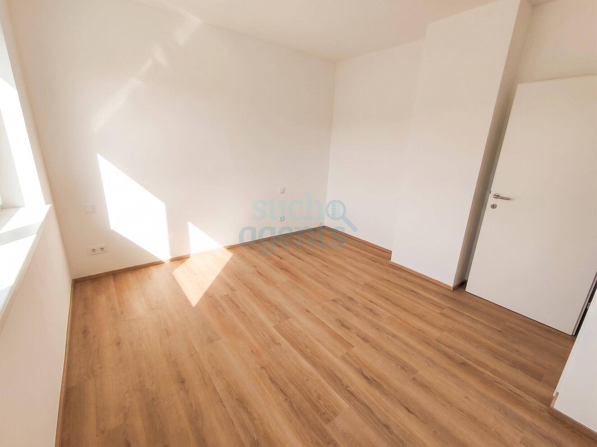 Helles, leeres Zimmer mit Laminatboden und viel Sonnenlicht, das durch das Fenster fällt.