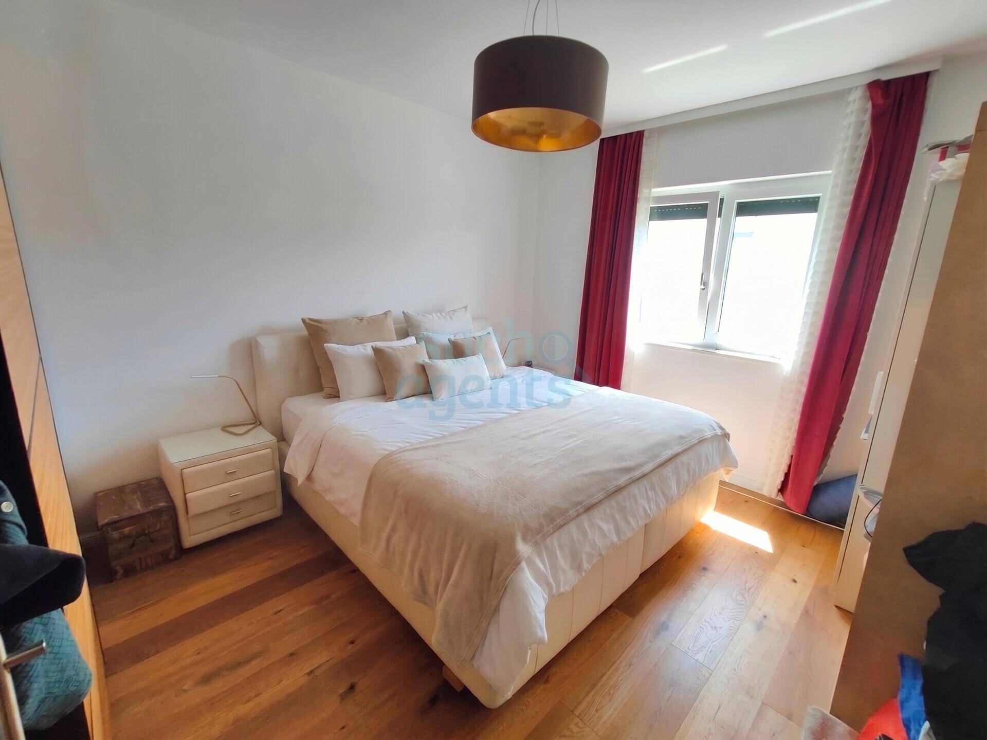 Gemütliches Schlafzimmer mit Doppelbett, Holzboden und Fenster mit roten Vorhängen.