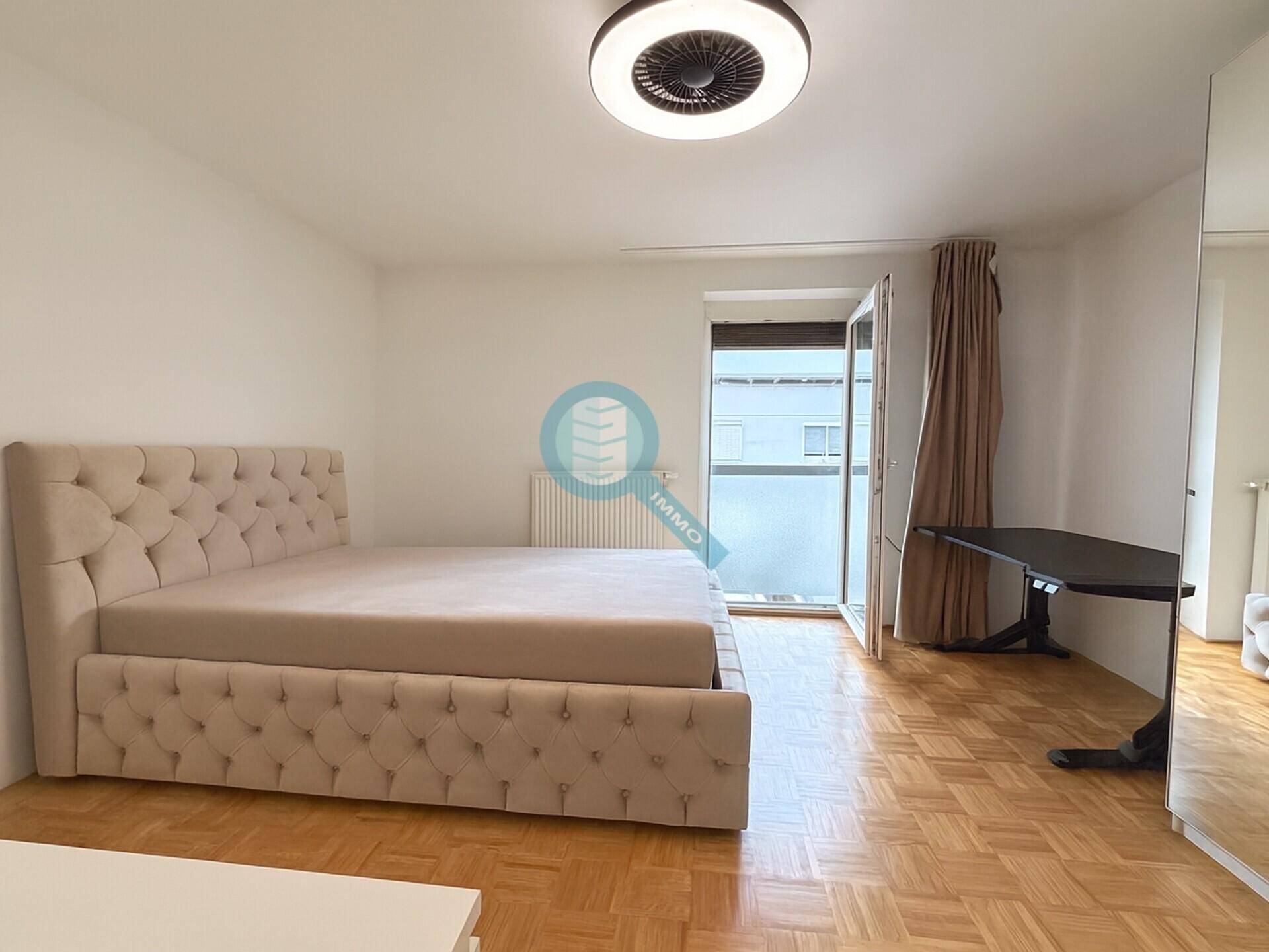 Geräumiges Schlafzimmer mit gepolstertem Bett, Parkettboden und Zugang zum Balkon.