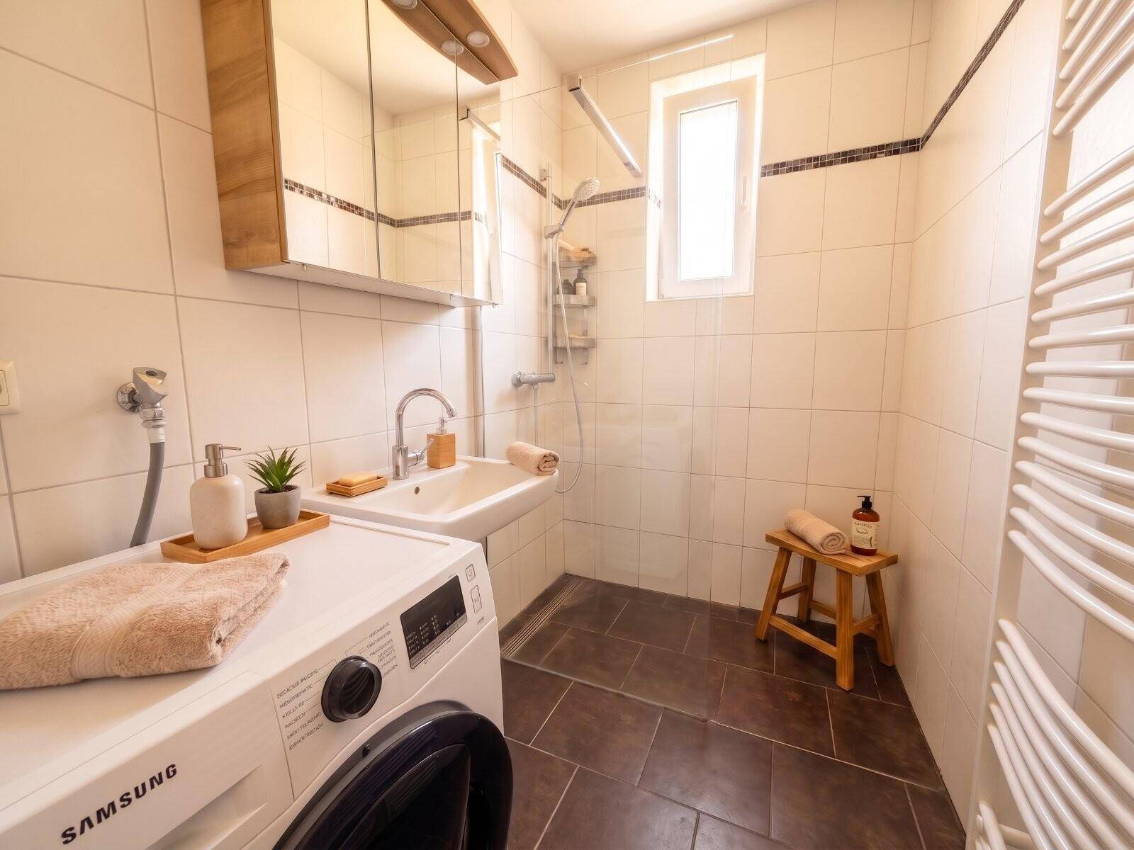 Modernes Badezimmer mit Dusche, Waschbecken, Waschmaschine, Fenster und Handtuchheizkörper.