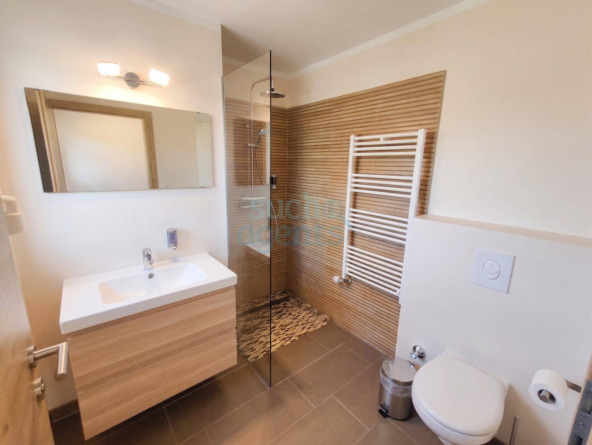 Modernes Badezimmer mit ebenerdiger Dusche, WC, Waschtisch mit Holzunterschrank und Handtuchheizkörper.