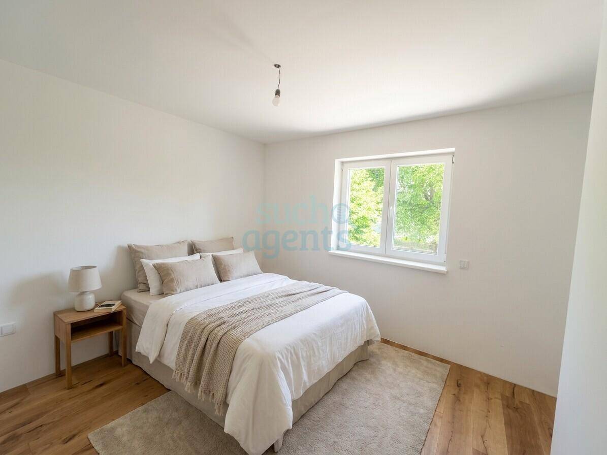 Freundliches Schlafzimmer mit Holzboden, großem Fenster und Blick ins Grüne.