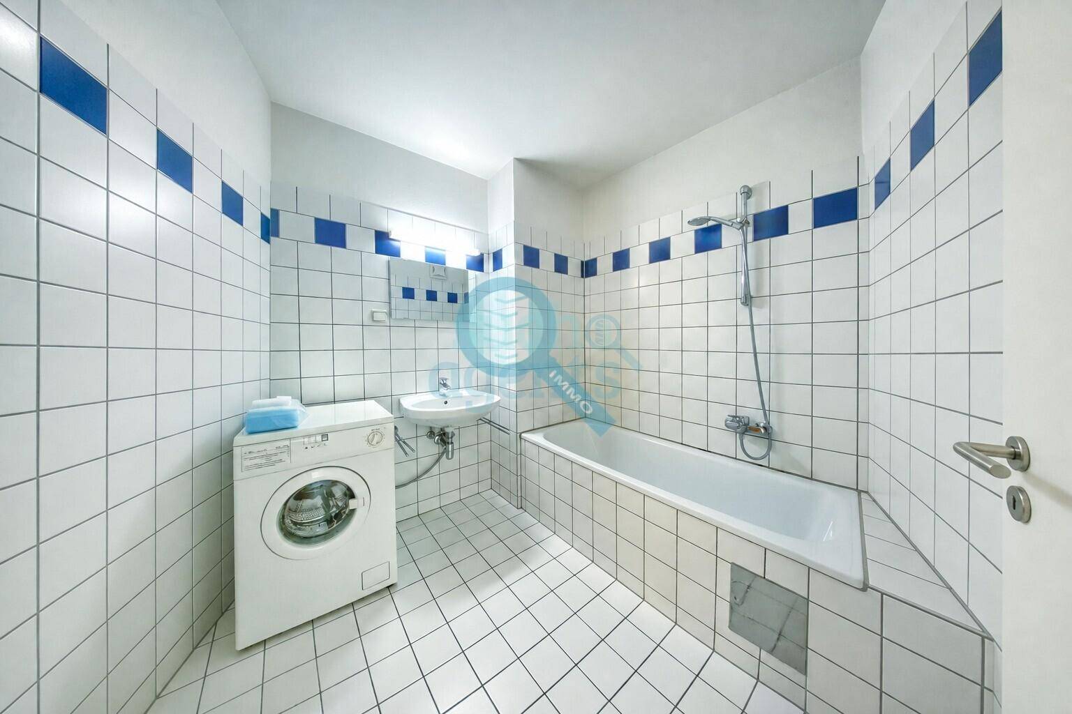 Badezimmer mit weißen und blauen Fliesen, Badewanne mit Duschfunktion und Waschmaschine.